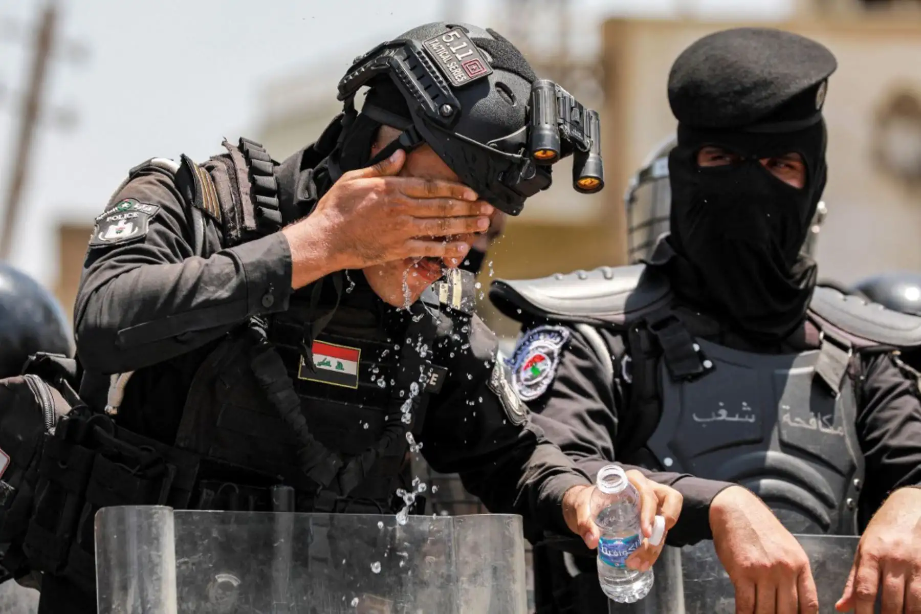 Un miembro de las fuerzas de seguridad iraquíes que hace guardia en una manifestación contra la escasez de agua y los cortes de energía se enjuaga la cara con agua de una botella para refrescarse en Bagdad. Foto: AFP