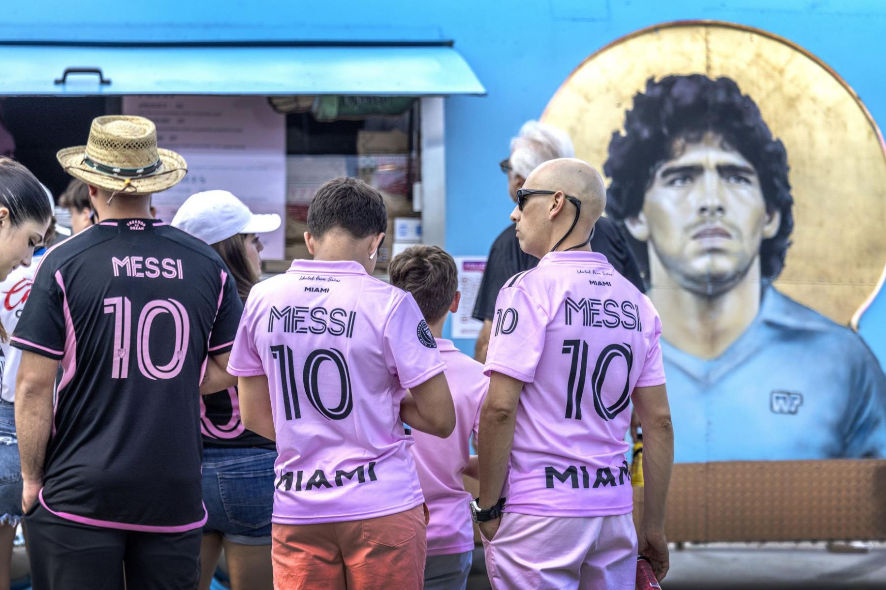 Los fanáticos del futbolista argentino Lionel Messi esperan en fila junto a una foto del futbolista argentino Diego Armando Maradona exhibida en un camión de comida antes del partido de la Copa de la Liga de Fútbol entre Cruz Azul e Inter Miami CF afuera del estadio DRV PNK en Fort Lauderdale, Florida, EE. UU., el 21 de julio del 2023. Foto: EFE