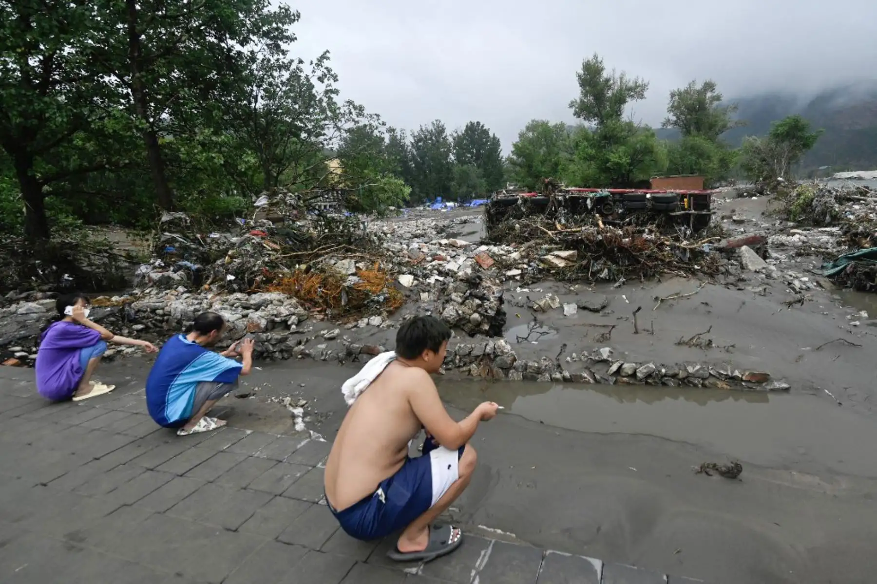 La gente mira un camión volcado luego de fuertes lluvias en el distrito de Fangshan en Beijing. Al menos 20 personas murieron y 19 desaparecieron después de que las fuertes lluvias azotaran Beijing, dijeron los medios estatales el 1 de agosto, en aguaceros que han sumergido carreteras y barrios inundados de lodo. Foto: AFP
