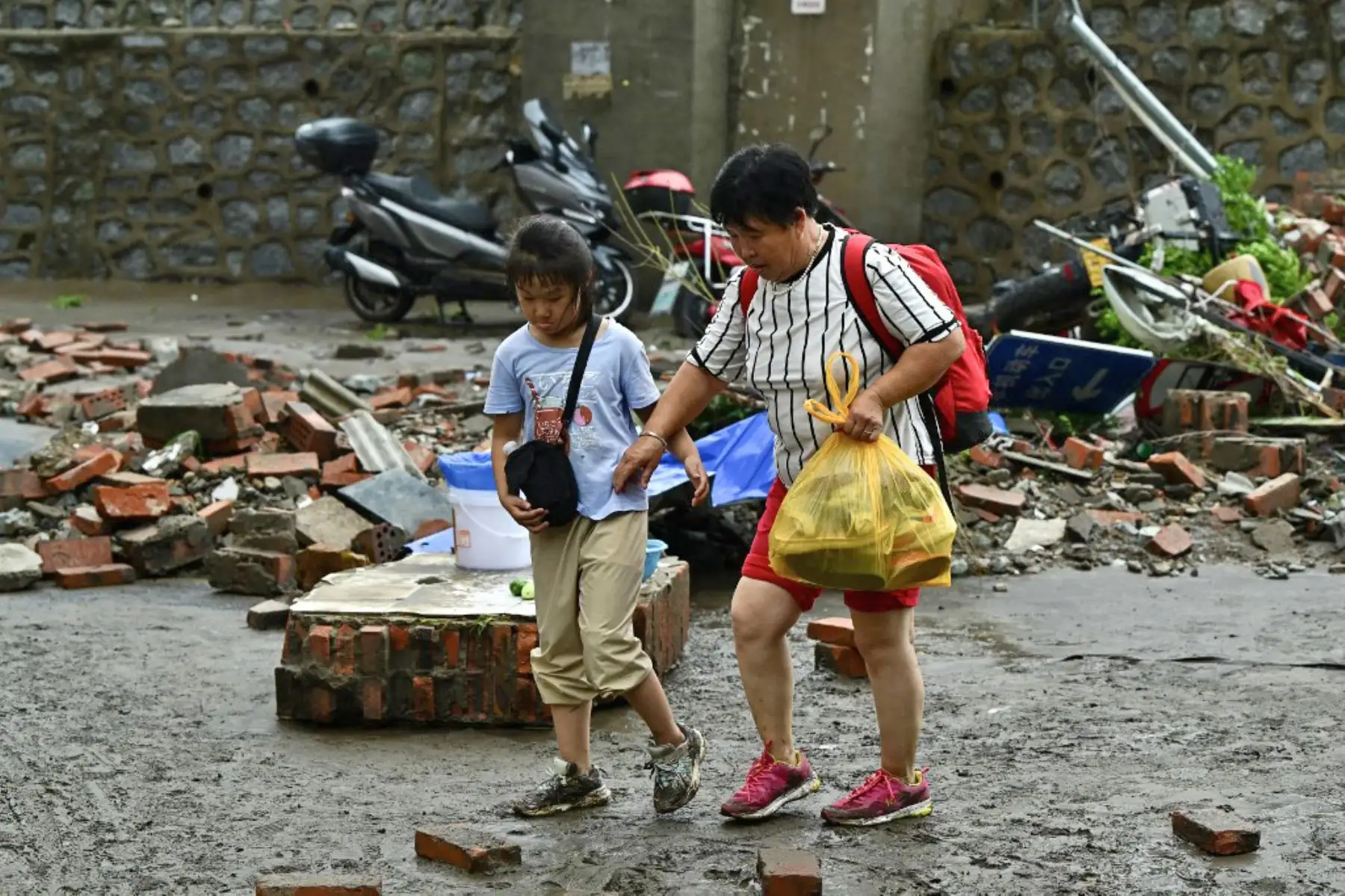 La gente se abre paso a través de una carretera dañada luego de las fuertes lluvias en el distrito de Fangshan en Beijing. Al menos 20 personas murieron y 19 desaparecieron después de que las fuertes lluvias azotaran Beijing, dijeron los medios estatales. Foto: AFP