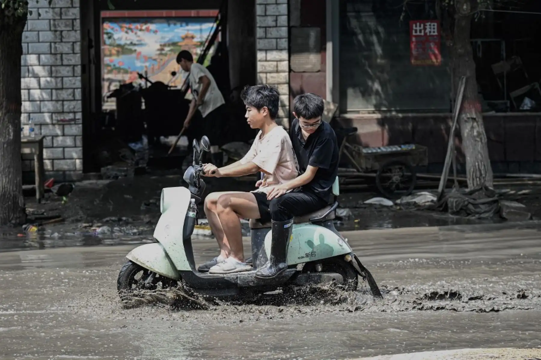 Los residentes locales viajan en scooter por una calle embarrada después de las inundaciones provocadas por las fuertes lluvias en la ciudad de Zhuozhou, en la provincia de Hebei, en el norte de China. Foto: AFP