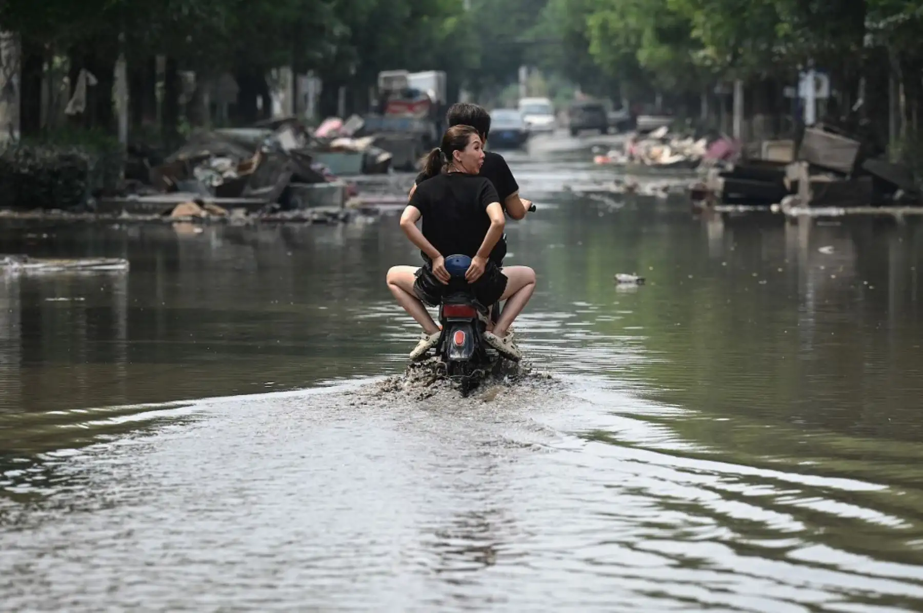 Los residentes locales viajan en scooter por una calle embarrada después de las inundaciones provocadas por las fuertes lluvias en la ciudad de Zhuozhou, en la provincia de Hebei, en el norte de China. Foto: AFP