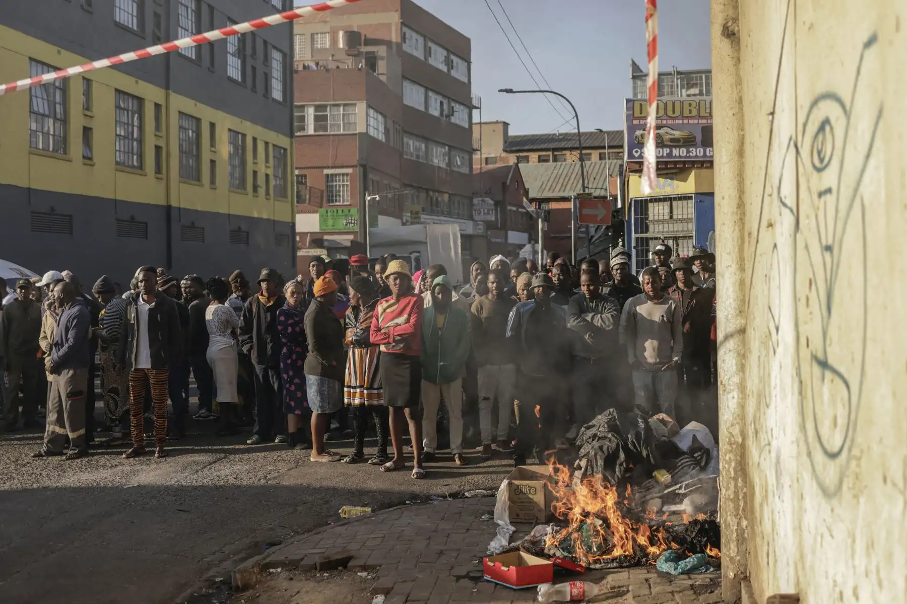 Las personas que se encuentran junto a una hoguera observan cómo los bomberos trabajan en la escena de un incendio en un edificio en Johannesburgo. Un incendio devoró un edificio de cinco pisos en el centro de Johannesburgo. Foto: AFP