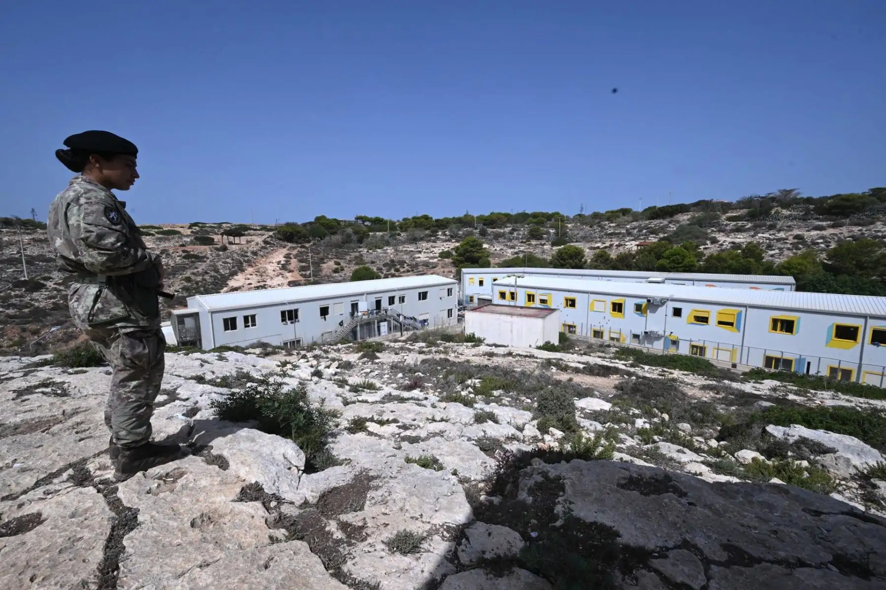 Miembros del ejército italiano se encuentran en una colina vigilando el centro de recepción de inmigrantes en Lampedusa, Italia. El perímetro está controlado por el ejército italiano. Foto: EFE