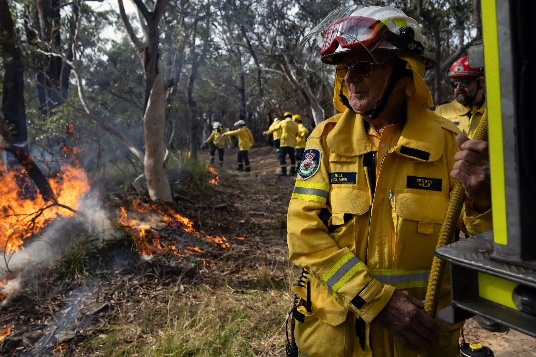 Esta fotografía tomada el 15 de julio de 2023 muestra al bombero voluntario Bill Holmes sacando una manguera de un camión durante una quema de reducción de peligros en el norte de Sydney. Foto: AFP
