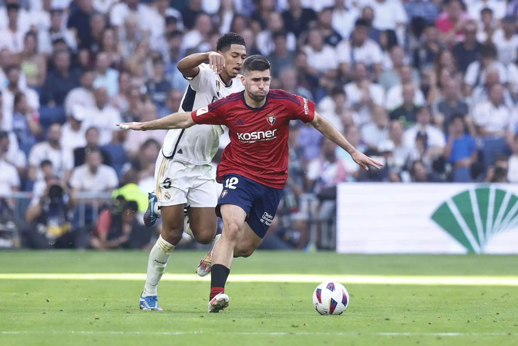 El defensa del Osasuna Jesús Areso  con el balón seguido por el centrocampista inglés del Real Madrid Jude Bellingham durante el partido de Liga EA Sports que el Real Madrid y el Osasuna disputan este sábado en el Estadio Santiago Bernabéu de Madrid.  Foto:ANDINA/EFE