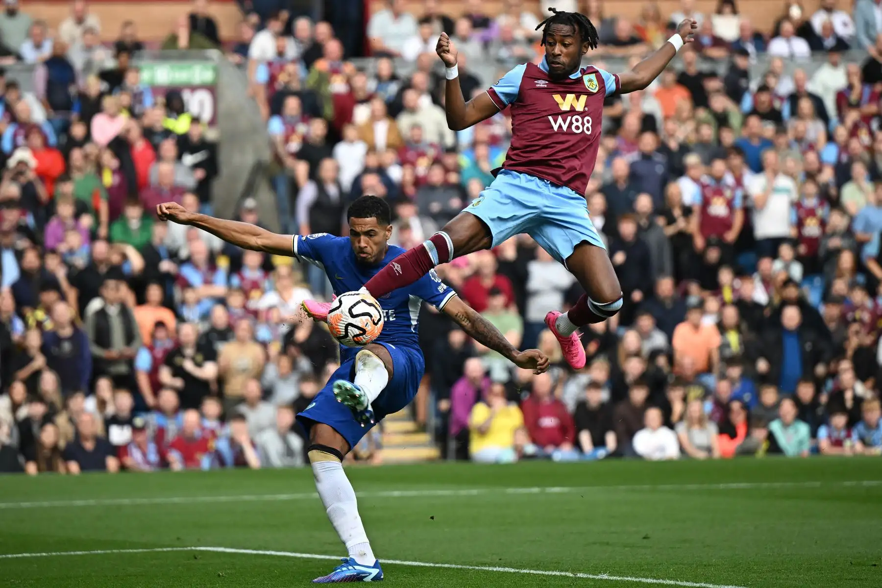 El mediocampista belga del Burnley  Mike Tresor  salta por encima del defensor inglés del Chelsea Levi Colwill mientras intenta un tiro a portería durante el partido de fútbol de la Premier League inglesa entre Burnley y Chelsea en Turf Moor en Burnley, noroeste de Inglaterra. Foto: ANDINA/AFP