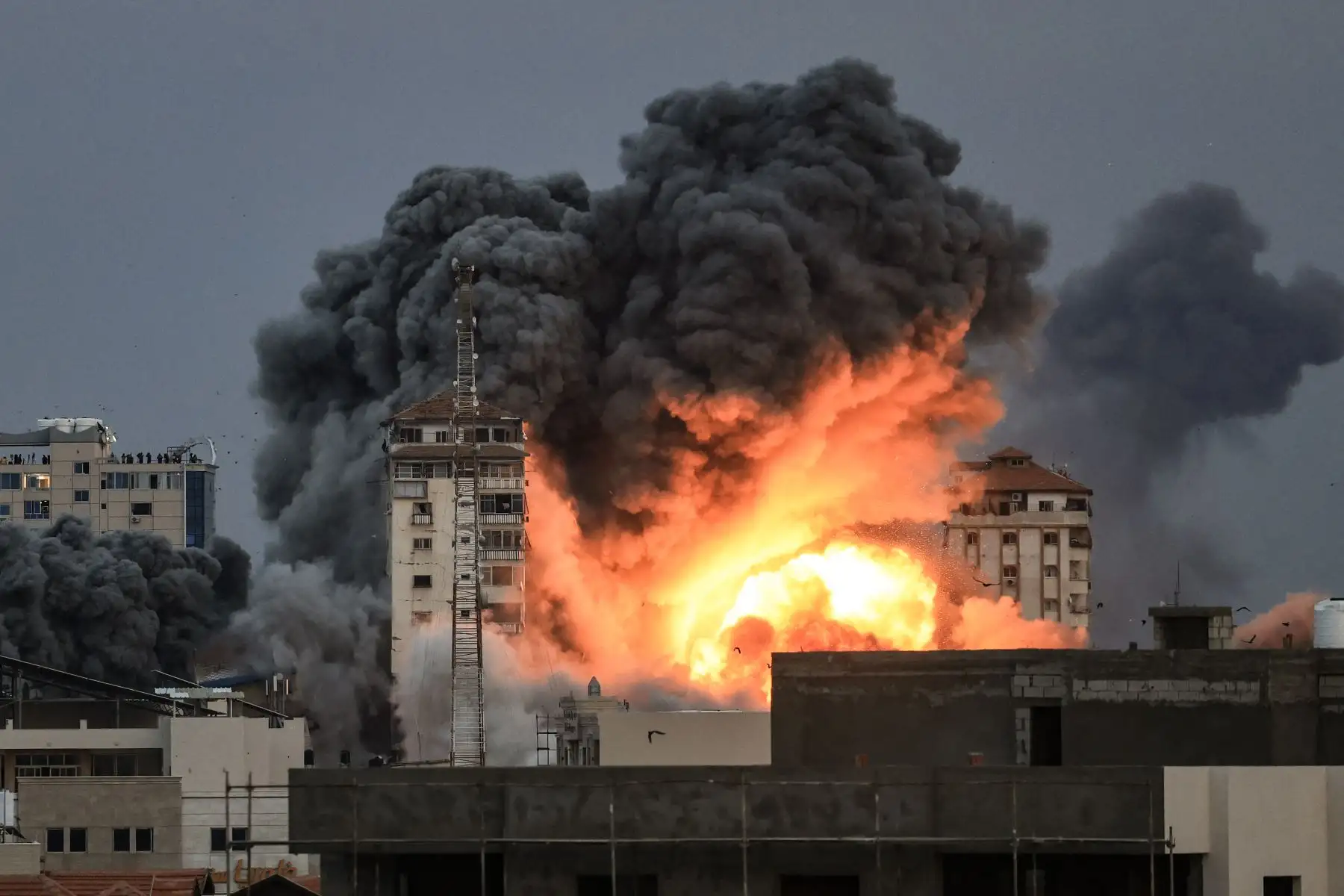 La gente parada en una azotea observa cómo una bola de fuego y humo se eleva sobre un edificio en la ciudad de Gaza el 7 de octubre de 2023 durante un ataque aéreo israelí que golpeó el edificio de la Torre Palestina. 
Foto: AFP