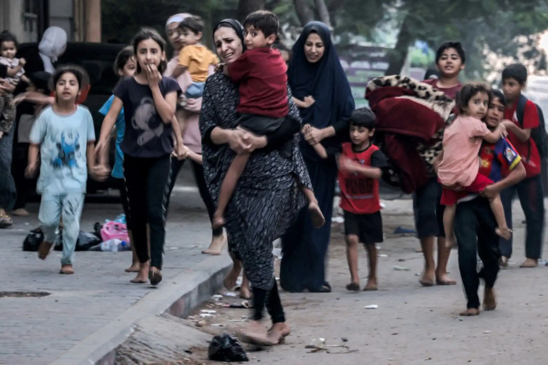 Mujeres palestinas con sus hijos que huyen de sus hogares tras los ataques aéreos israelíes corren por una calle de la ciudad de Gaza. Foto: AFP