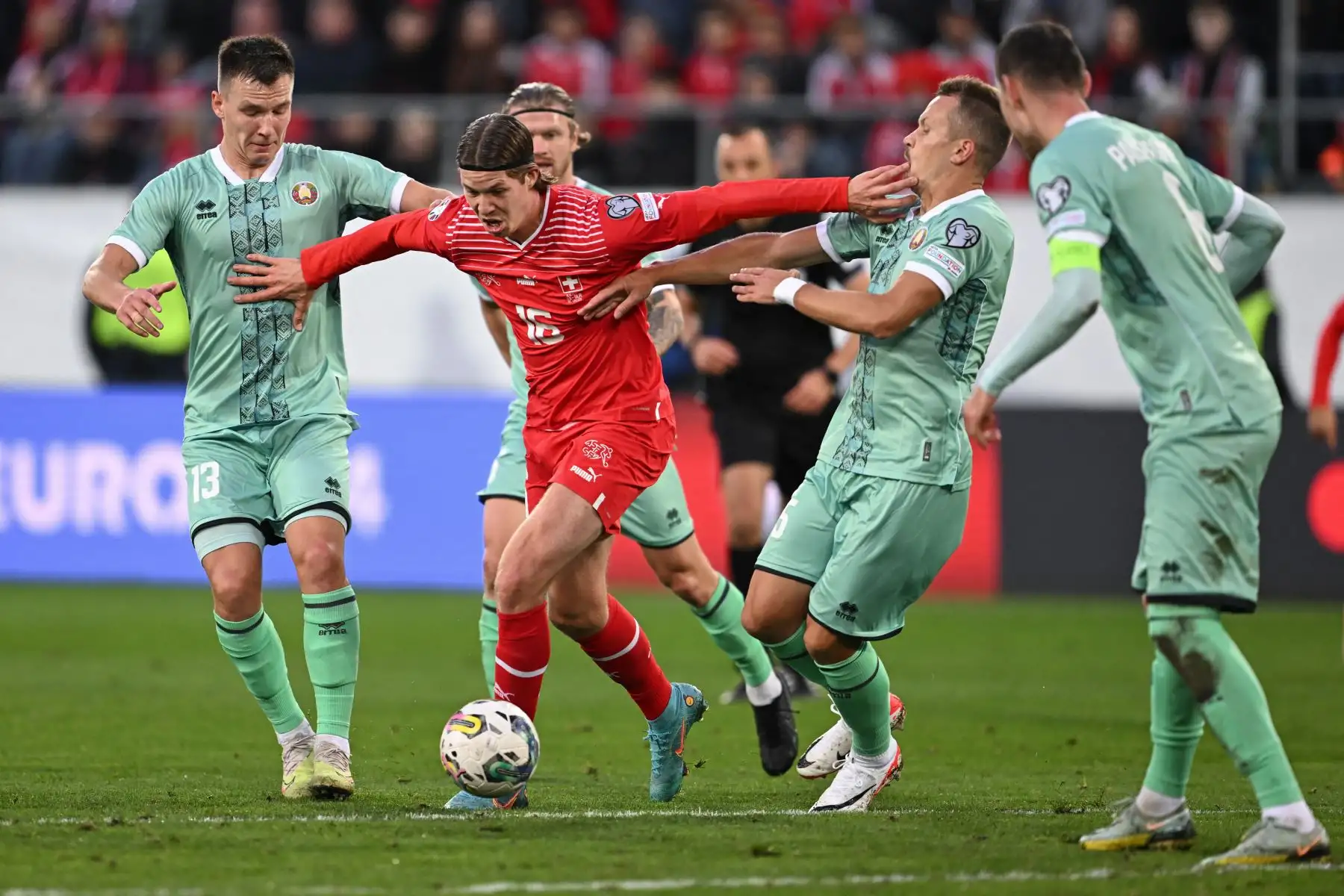 El delantero suizo  Cedric Itten  lucha por el balón con el centrocampista bielorruso Valeri Bocharov  y el defensor bielorruso Denis Polyakov  durante el partido de clasificación del Grupo I del torneo de fútbol de la UEFA Euro 2024 entre Suiza y Bielorrusia. en el estadio Kybunpark de St. Gallen. Foto. ANDINA/ AFP