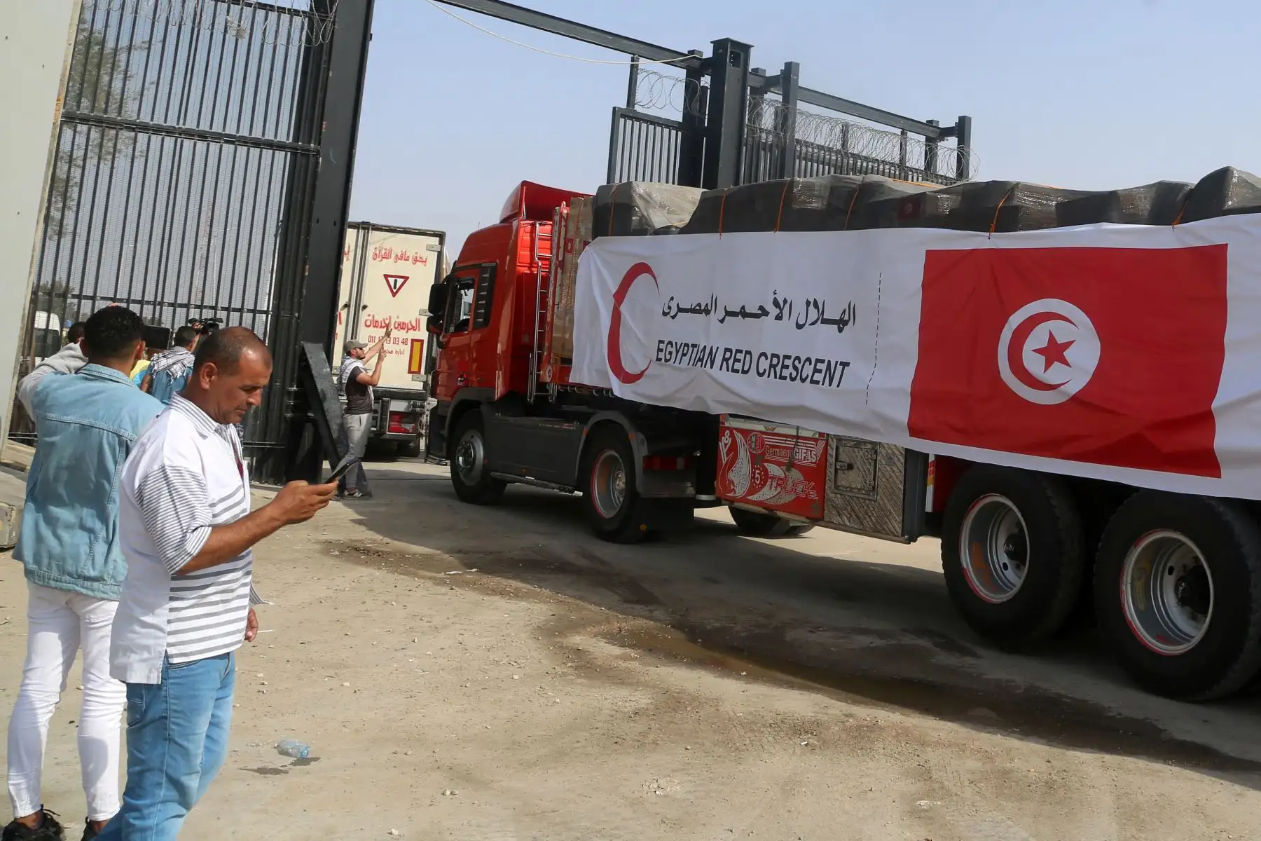 La gente en el lado egipcio del cruce fronterizo de Rafah observa cómo un convoy de camiones que transportan ayuda humanitaria cruza hacia la Franja de Gaza.
Foto: AFP