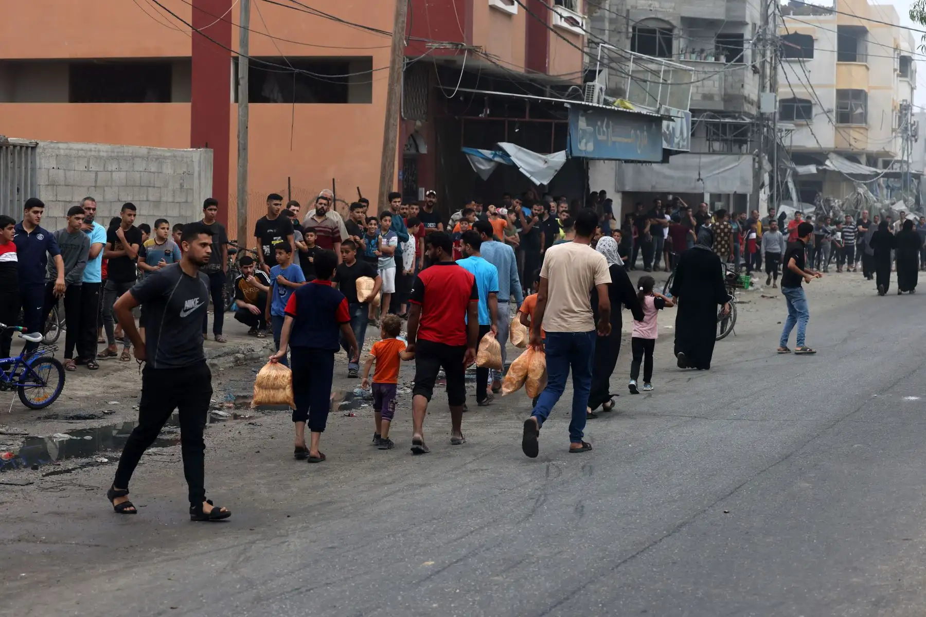 La gente lleva bolsas de pan mientras otros hacen cola frente a una panadería, después de los ataques israelíes en la ciudad de Gaza, Los ataques aéreos israelíes destruyeron cientos de edificios en la Franja de Gaza durante la noche, la población civil dijo el servicio de defensa en el territorio palestino controlado por Hamás. Foto: ANDINA/AFP