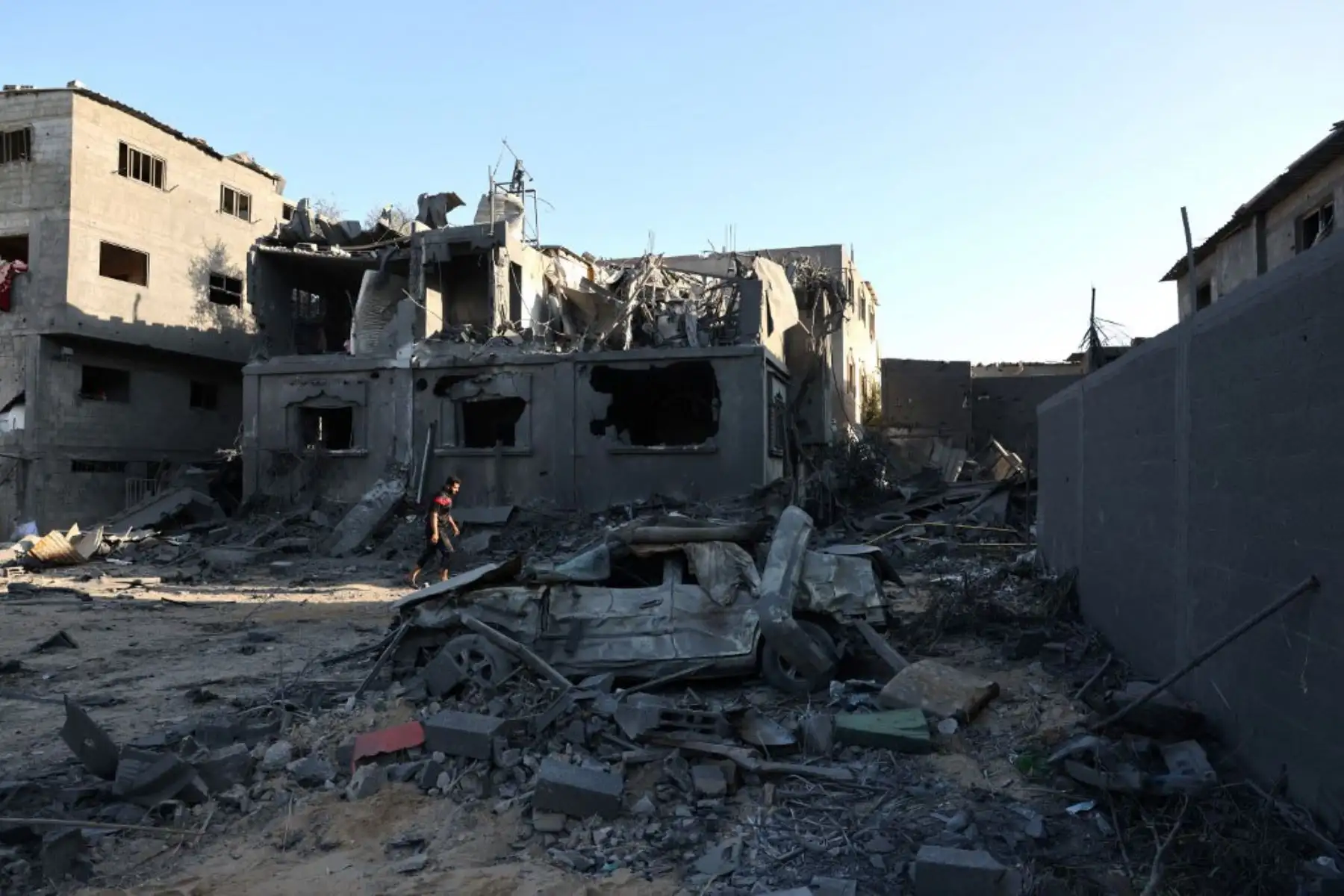 Palestinos pasan junto a una casa y un vehículo destruidos el día después de un ataque aéreo israelí contra el campo de refugiados de Nuseirat, en el centro de la Franja de Gaza. Foto: AFP