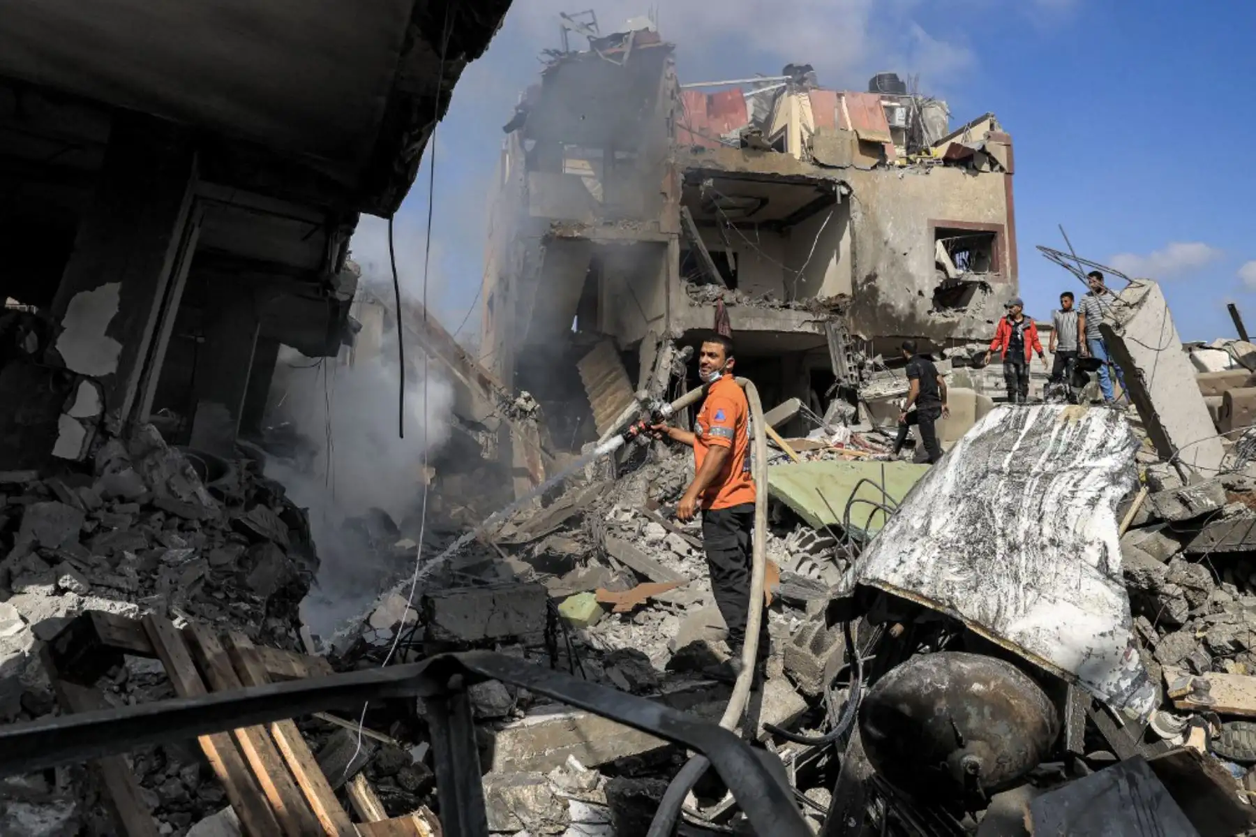 Un miembro de la defensa civil palestina rocía un edificio con una manguera para apagar un incendio en un edificio derrumbado después del bombardeo israelí en Khan Yunis, en el sur de la Franja. Foto: AFP