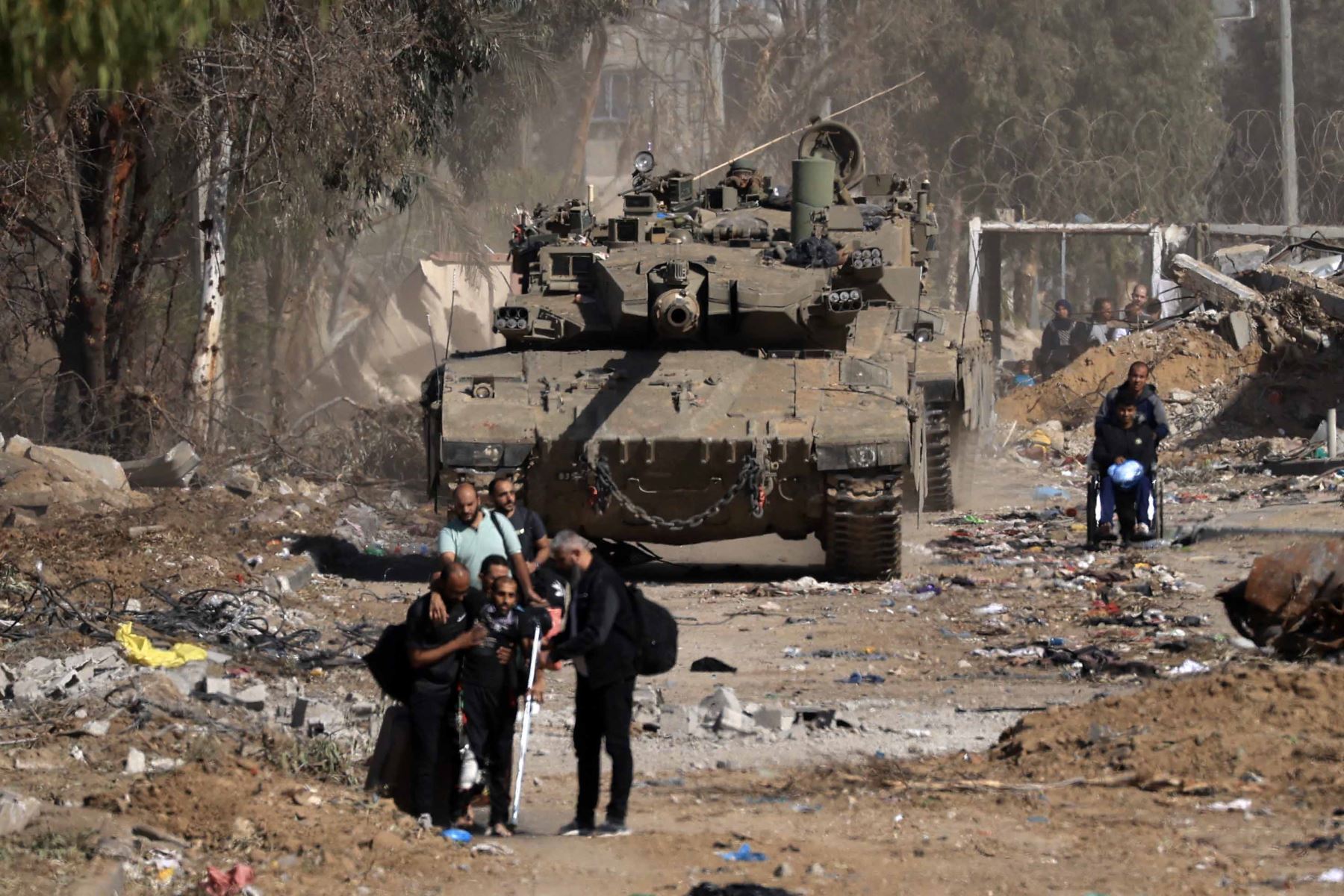 Los palestinos, incluidas las personas heridas durante el bombardeo, pasan junto a un tanque israelí mientras huyen hacia el norte a través de la carretera Salaheddine en el distrito de Zeitoun, en las afueras del sur de la ciudad de Gaza. Foto: AFP