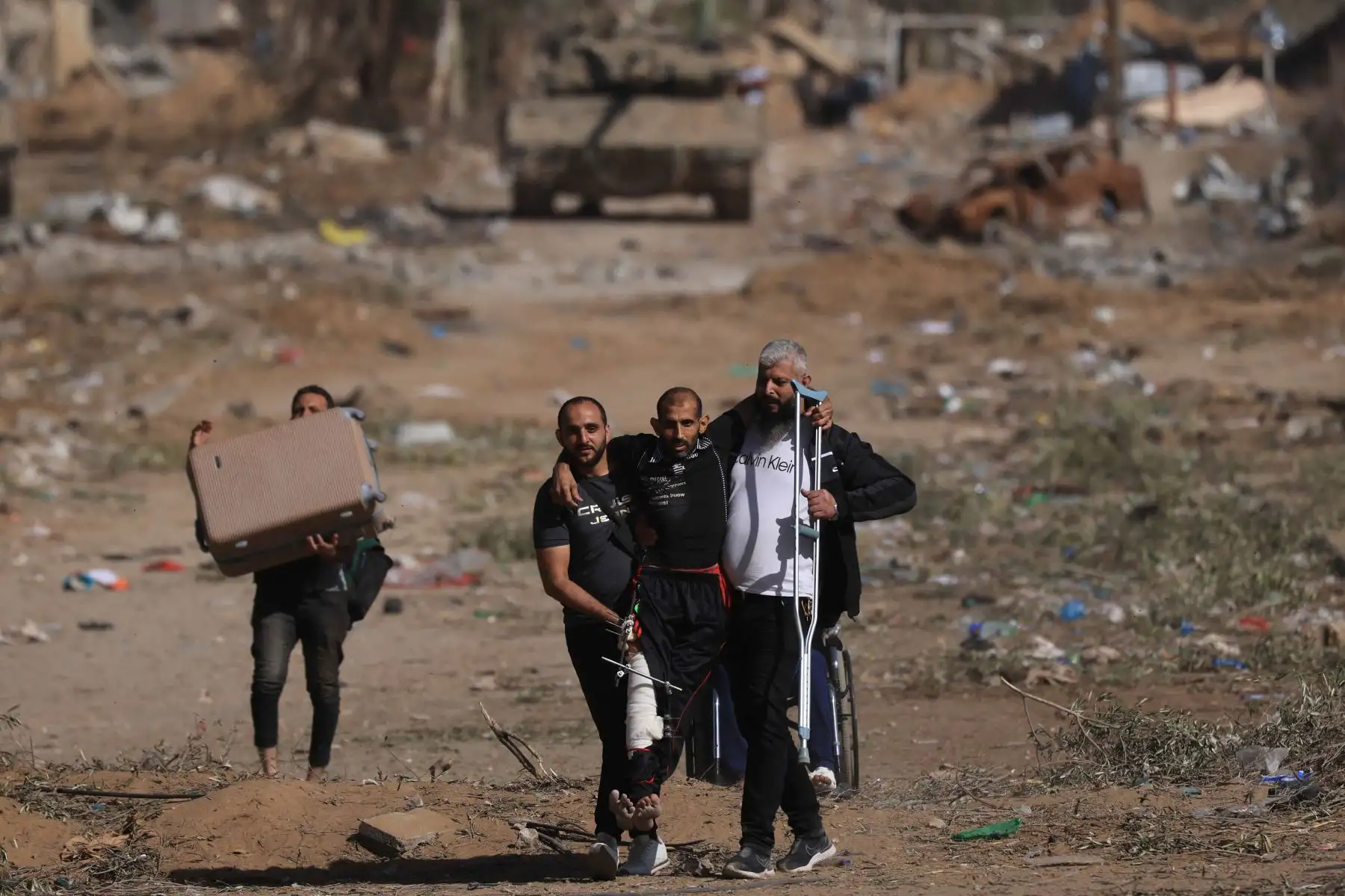 Los palestinos que huyen del norte por la carretera Salaheddine ayudan a un hombre herido mientras caminan frente a un tanque del ejército israelí en el distrito de Zeitoun, en las afueras del sur de la ciudad de Gaza, el 24 de noviembre de 2023, después de un  alto el fuego de varios días. Foto: AFP