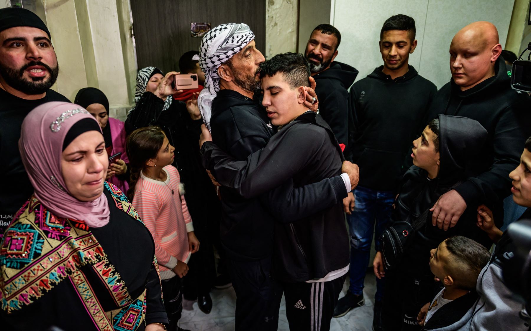 Ahmad Salaima, un palestino de 14 años liberado bajo un acuerdo de tregua ampliado, abraza a su padre mientras su madre observa su casa en Jerusalén Este, anexada por Israel, Con la policía israelí imponiendo una prohibición de Durante las celebraciones relacionadas con el regreso de los prisioneros palestinos en Jerusalén Este. Foto: ANDINA/AFP