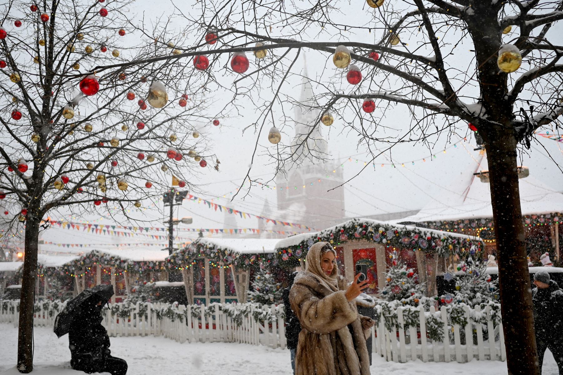 Una mujer se toma una selfie frente a los puestos del mercado navideño y la torre Spasskaya del Kremlin en la Plaza Roja cubierta de nieve en Moscú.
Foto: AFP