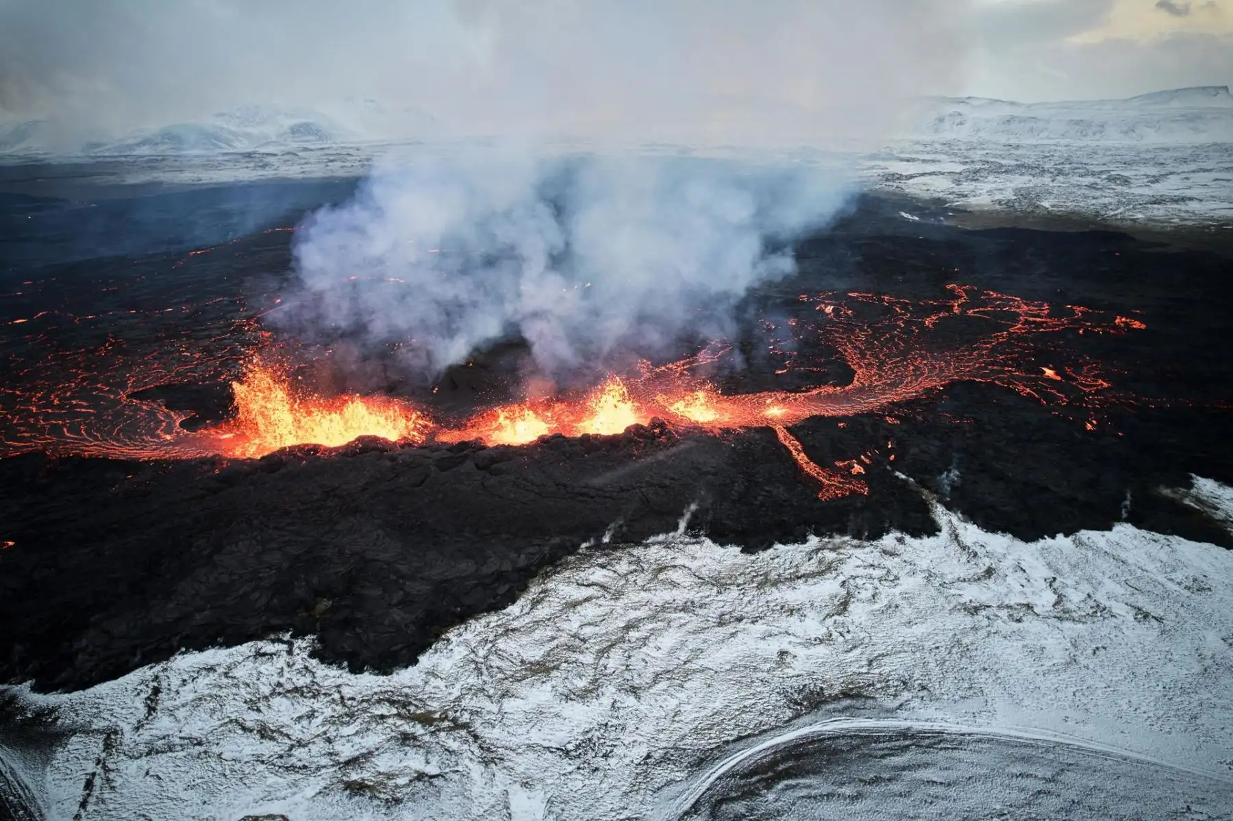 Una vista aérea tomada con un drone muestra lava y humo arrojados de una fisura volcánica durante una erupción, cerca de la ciudad de Grindavik, en la península de Reykjanes, al suroeste de Islandia, el 19 de diciembre de 2023. La Oficina Meteorológica de Islandia (OMI) anunció el inicio de una erupción de fisura volcánica cerca del cráter Sundhnuka, al noreste de Grindavik, la noche del 18 de diciembre, tras semanas de intensa actividad sísmica en la zona. La potencia y la actividad sísmica de la erupción han disminuido con el tiempo, informó la OMI el 19 de diciembre, añadiendo que desde que comenzó la erupción se han registrado unos 320 terremotos.

Foto: EFE