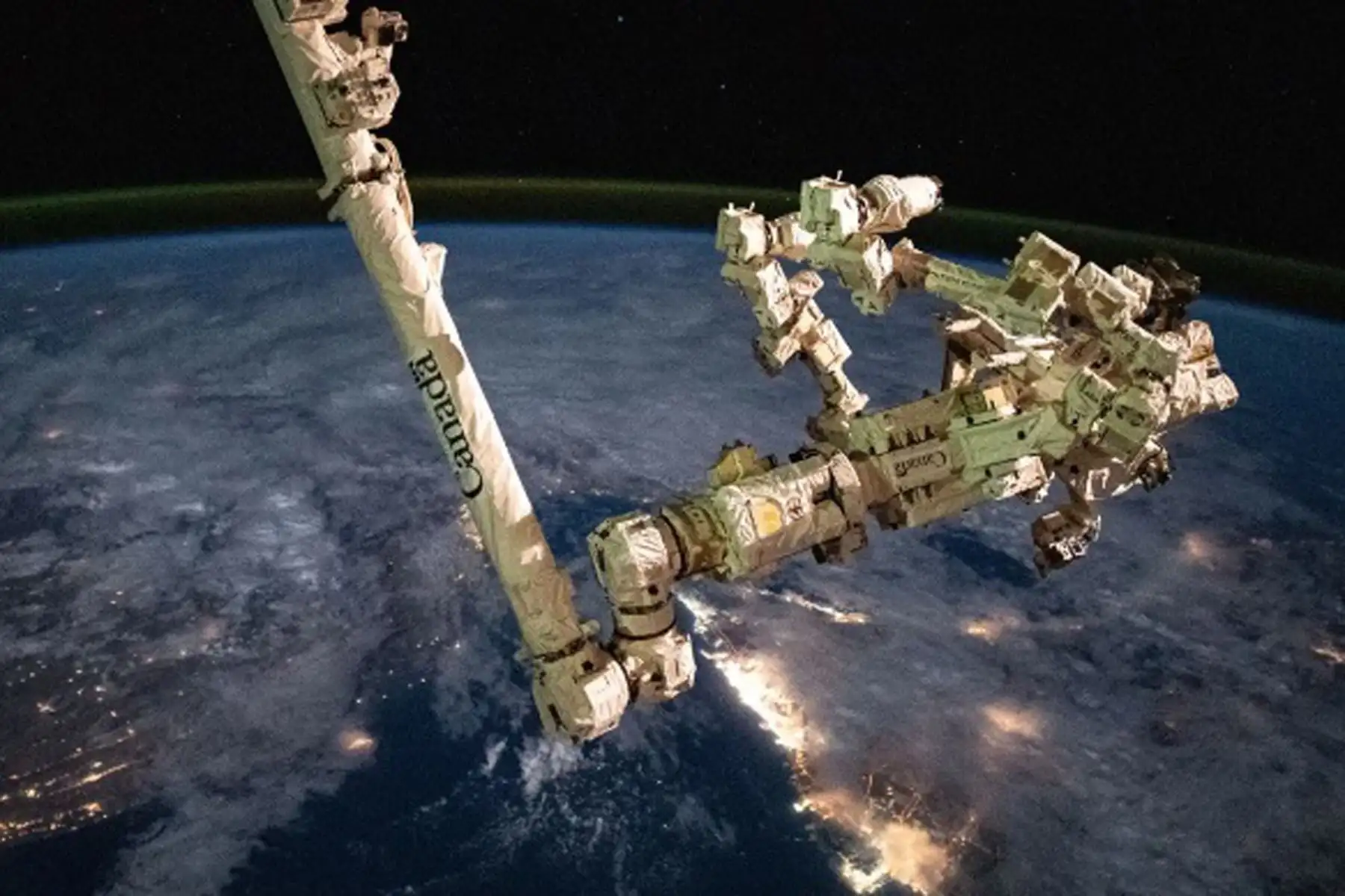 El brazo robótico Canadarm2, con su mano robótica Dextre acoplada a él, es fotografiado mientras la Estación Espacial Internacional orbita a 418 kilómetros (260 millas) de altura sobre las luces de las ciudades de la península arábiga. Canadarm2 es utilizado para instalar experimentos fuera de la estación espacial de forma remota. 
Foto: NASA