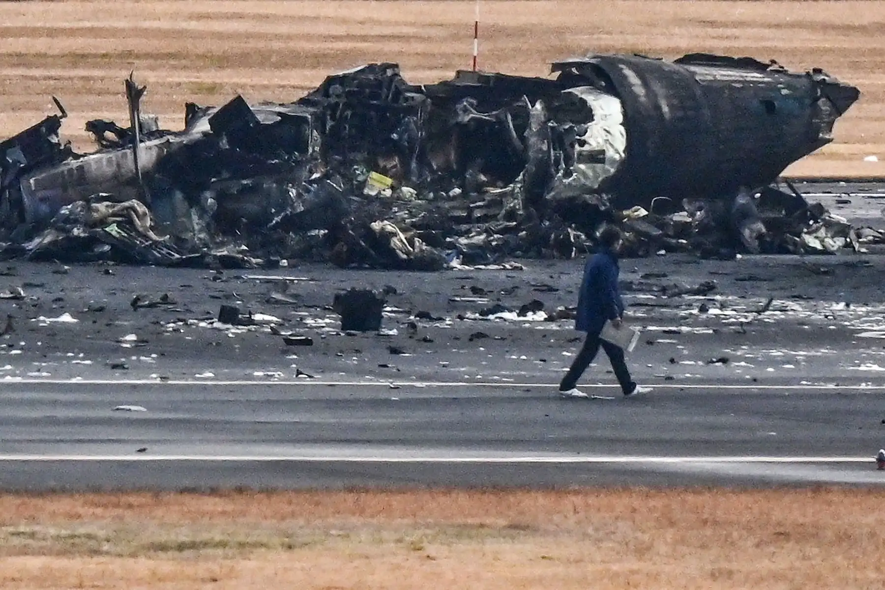 Un funcionario observa los restos de un avión de la Guardia Costera de Japón en la pista del Aeropuerto Internacional de Tokio en Haneda en Tokio.
Foto: AFP