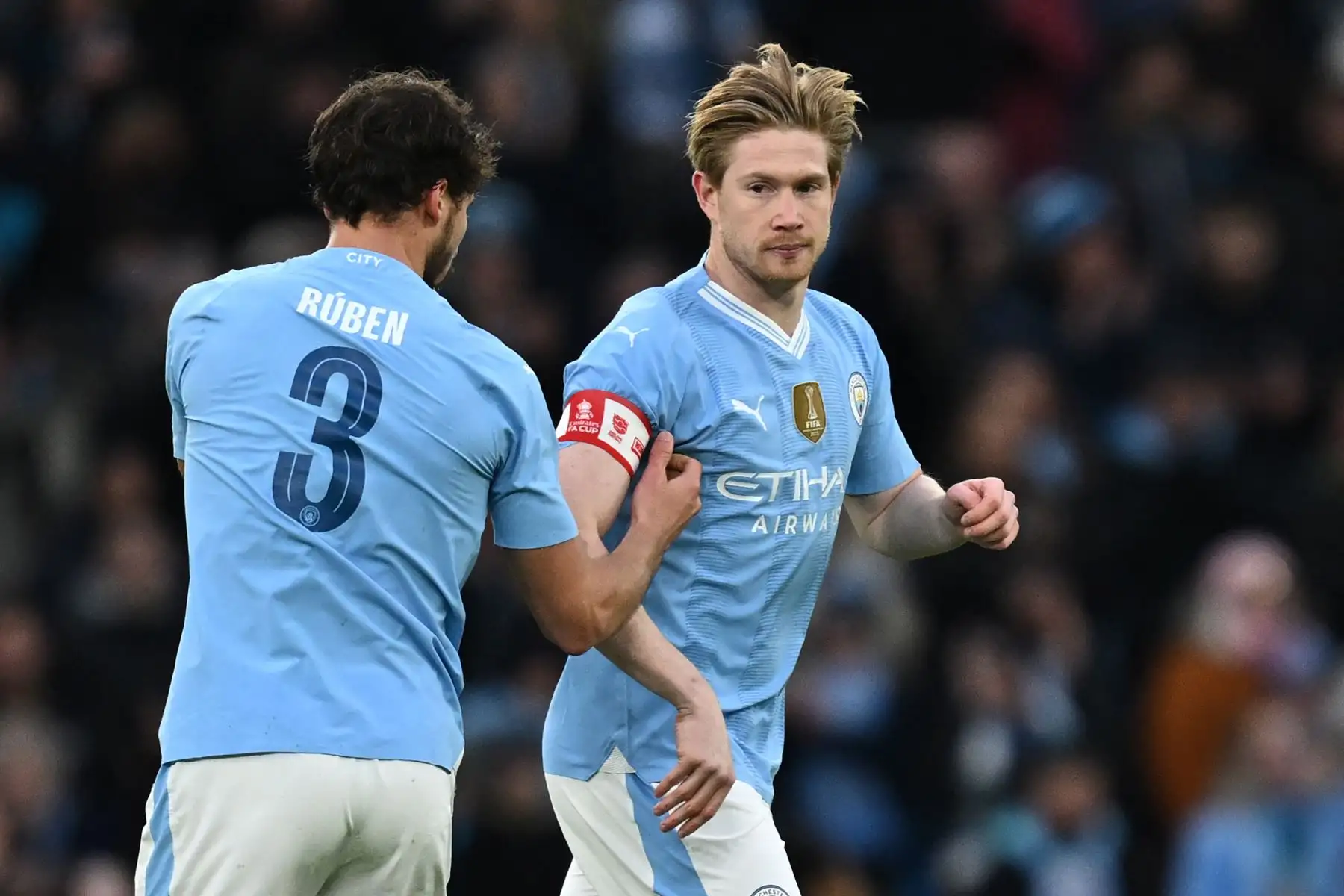 El defensor portugués del Manchester City Ruben Dias  pasa el brazalete de capitán al centrocampista belga del Manchester City Kevin De Bruyne durante el partido de fútbol de la tercera ronda de la Copa FA inglesa entre Manchester City y Huddersfield Town en el estadio Etihad de Manchester. noroeste de Inglaterra. Foto: ANDINA/AFP