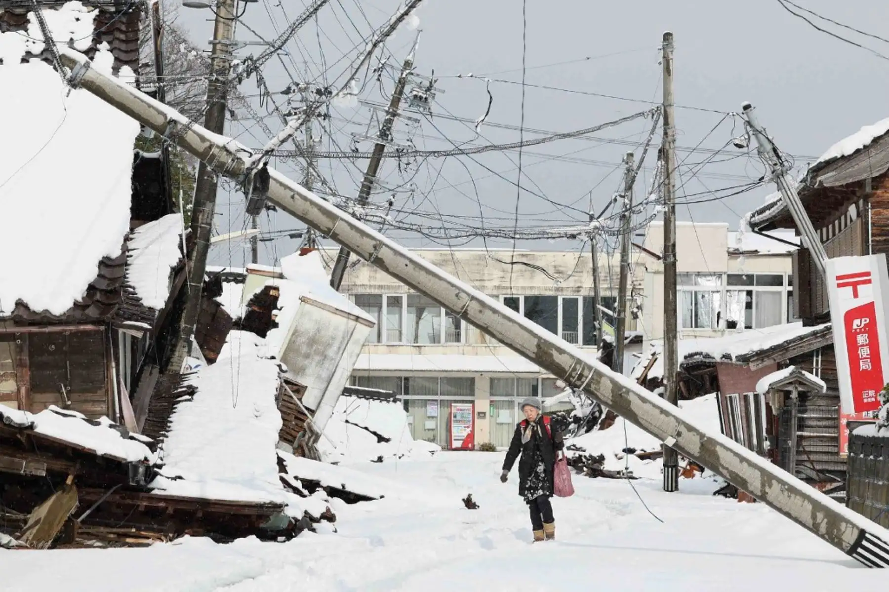 Una mujer caminan bajo un poste de servicios públicos caído después de que la nieve cubriera el área afectada por el desastre en la ciudad de Suzu, prefectura de Ishikawa, una semana después de que un gran terremoto de magnitud 7,5 sacudiera la región de Noto en la prefectura de Ishikawa el día de Año Nuevo. Foto: AFP