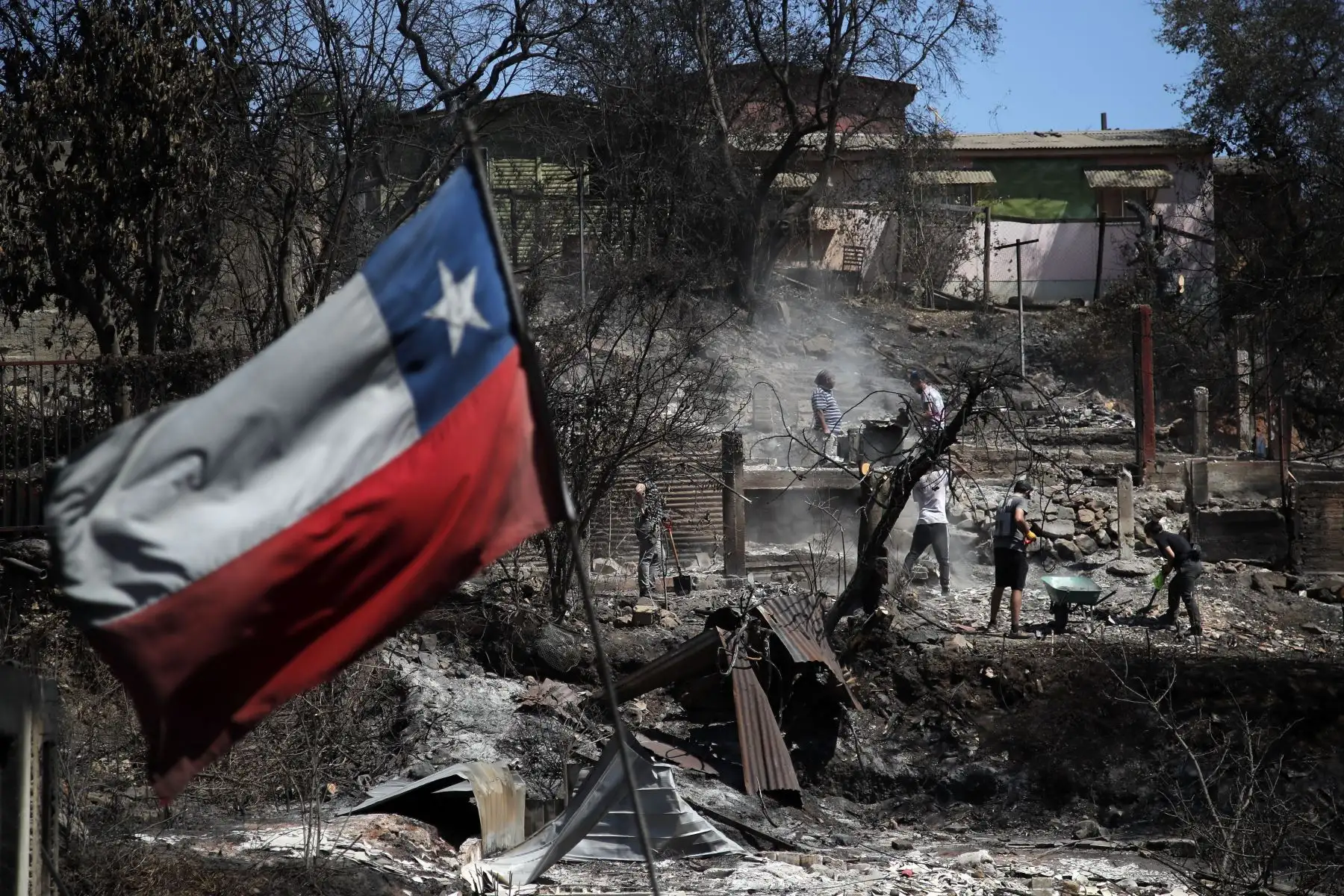 Una bandera chilena ondea mientras los vecinos limpian sus tierras y queman casas en Villa Independencia, región de Valparaíso, El número de muertos por los incendios forestales en el centro de Chile ascendió a al menos 112 personas el domingo, después de que el presidente Gabriel Boric advirtiera el número aumentaría "significativamente" a medida que los equipos busquen en los barrios destruidos. Foto: ANDINA/AFP