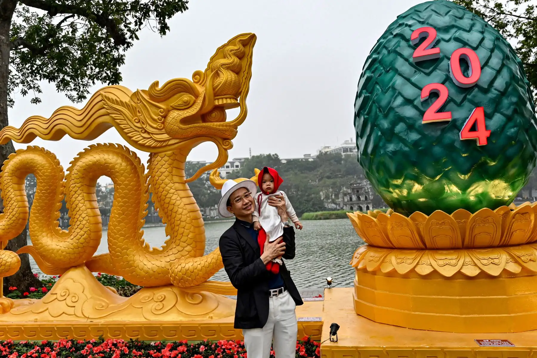 Un hombre posa para una foto con su hijo frente a una instalación con forma de dragón en el lago Hoan Kiem en Hanoi el 6 de febrero de 2024, mientras los vietnamitas se preparan para celebrar su tradicional Tet o Año Nuevo Lunar del Dragón. Foto: ANDINA/AFP