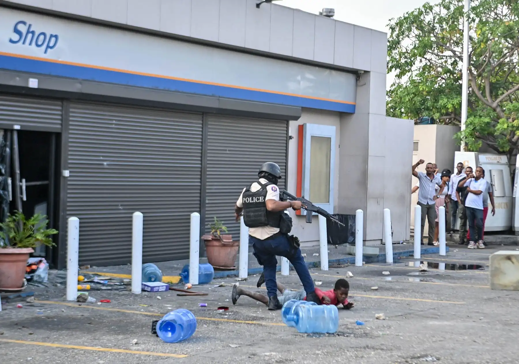 Q Un policía haitiano patea a un niño mientras la gente saquea una tienda de comestibles durante una manifestación que pide la salida del Primer Ministro haitiano Ariel Henry. Foto: ANDINA/ AFP