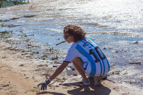 Fotografía cedida por Join The Planet donde aparece una mujer vistiendo la camiseta del astro argentino del fútbol Lionel Messi, mientras recoge botellas de plástico del río Paraná en Rosario (Argentina). Foto: EFE
