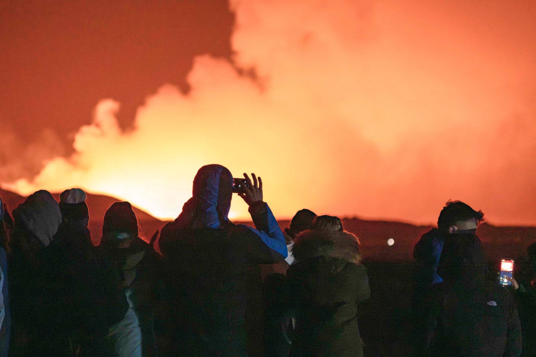 La gente se reúne para observar cómo la lava fundida fluye desde una fisura en la península de Reykjanes, al norte de la ciudad evacuada de Grindavik, en el oeste de Islandia. Lava arrojada el sábado desde una nueva fisura volcánica en la península de Reykjanes en Islandia, la cuarta erupción en afectar el área desde diciembre, dijeron las autoridades. Foto: AFP