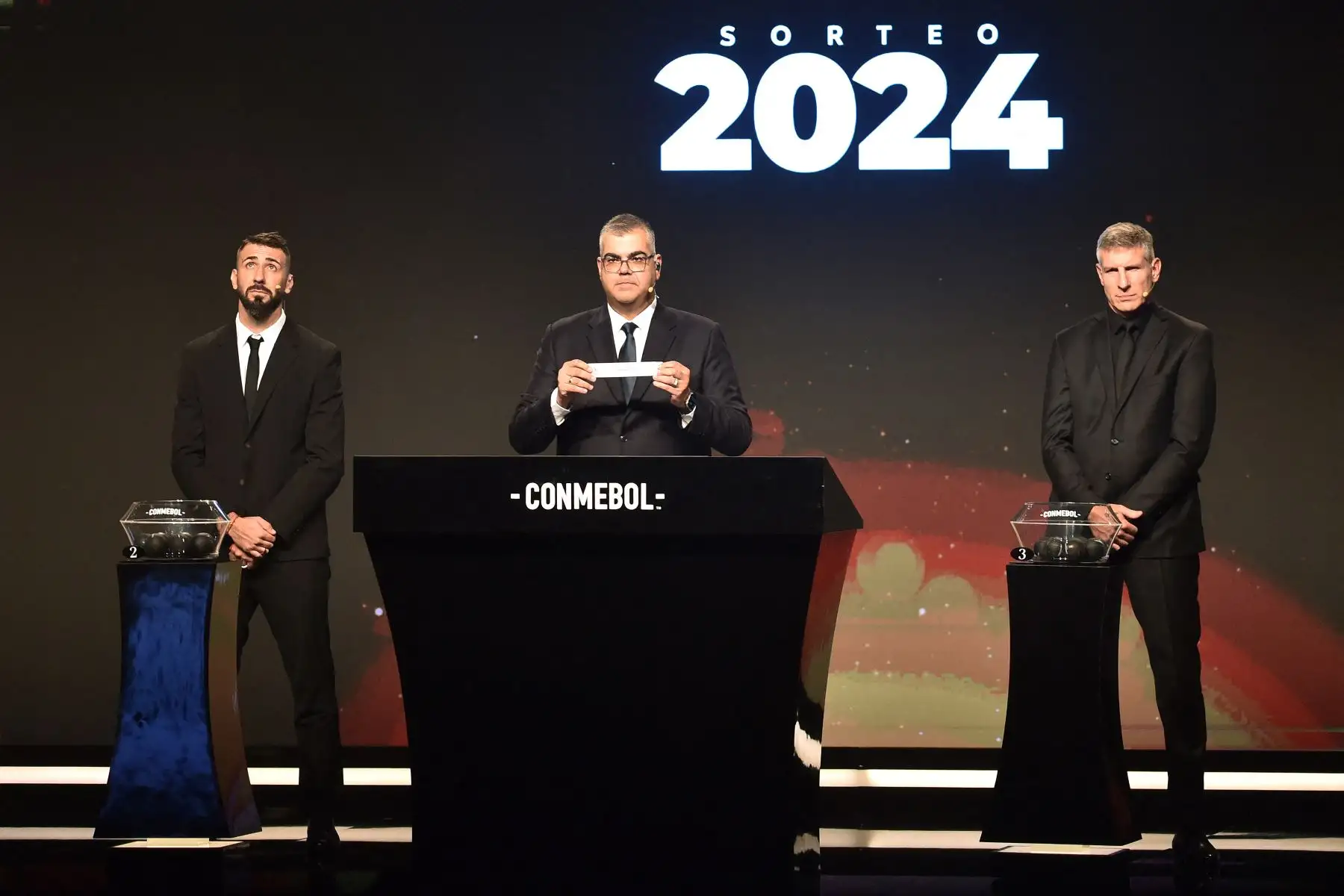 El Director de Competiciones de Clubes de la Conmebol, Frederico Nantes , muestra un desliz junto al delantero argentino Lucas Pratto  y al exfutbolista argentino Martín Palermo durante el sorteo de la Copa Libertadores en la sede de la Conmebol en Luque, Paraguay.
Foto: AFP