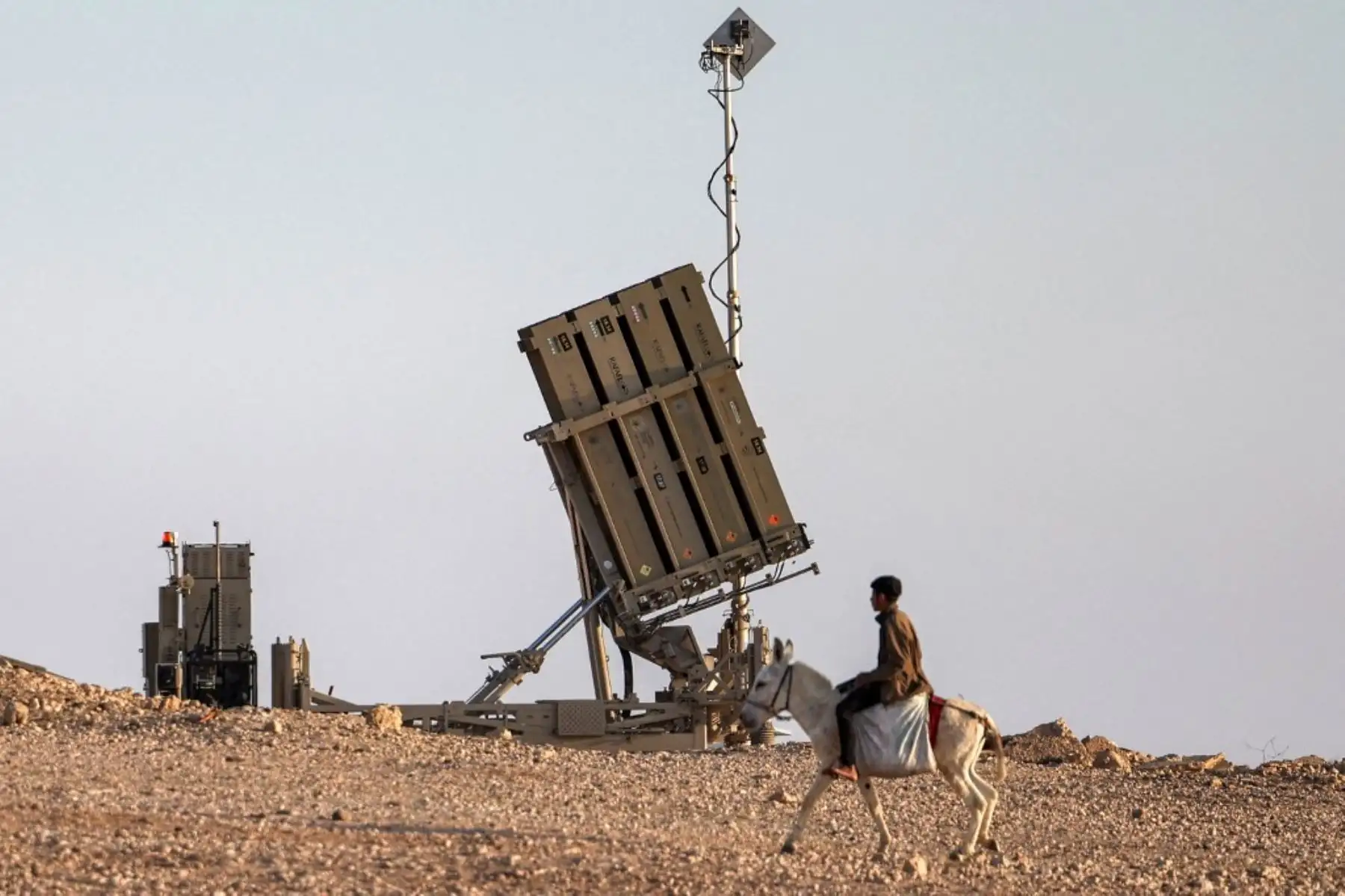 Un niño monta un burro cerca de una de las baterías del sistema de defensa antimisiles Cúpula de Hierro de Israel en una aldea no reconocida por las autoridades israelíes en el desierto del sur de Negev el 14 de abril de 2024. Foto: AFP
