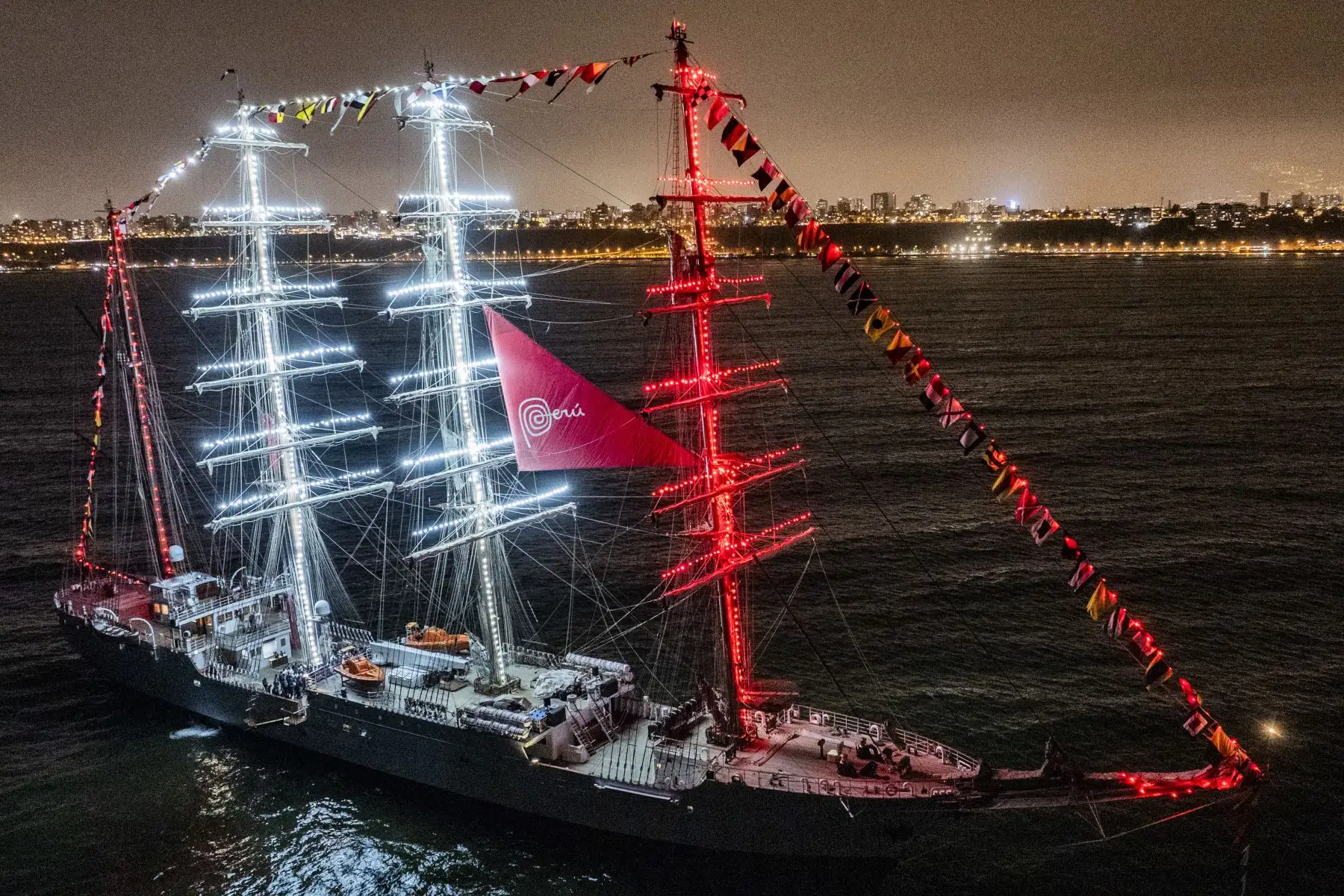 El Buque escuela B.A.P. Unión luce imponente frente a la costa de Chorrillos iluminado de rojo y blanco. Un gran espectáculo de fuegos artificiales le dio la bienvenida tras recorrer 36,400 millas náuticas y 317 días de viaje. Foto: Cortesía/Cristian Olea