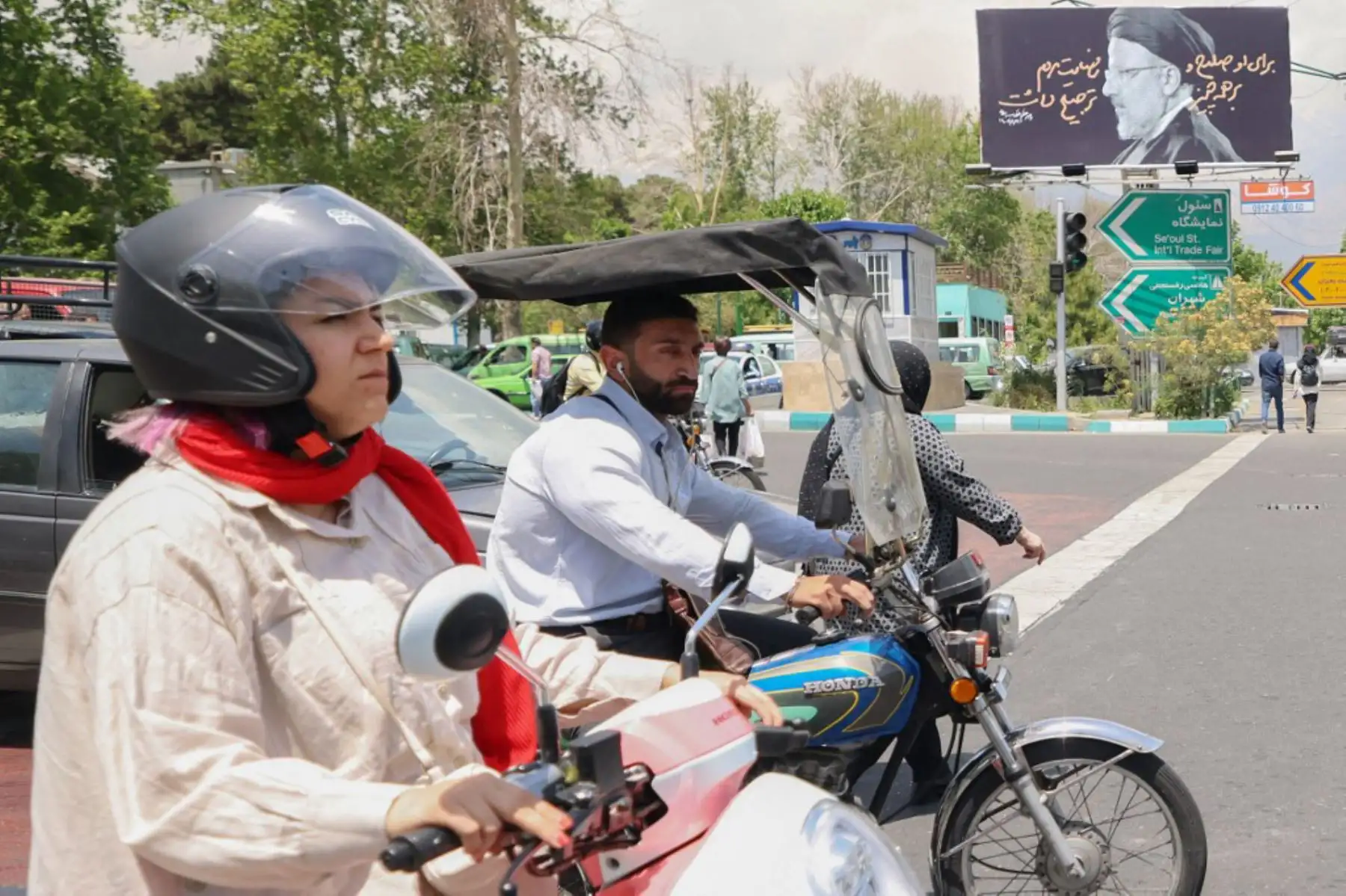 Un hombre y una mujer pasan en sus motocicletas junto a un cartel al fondo con un retrato del difunto presidente de Irán, Ebrahim Raisi, en el centro de Teherán, mientras los dolientes en la ciudad nororiental de Tabriz asistían a una procesión fúnebre para el presidente y su séquito que murieron en un accidente de helicóptero hace dos días. 
Foto. ANDINA/AFP