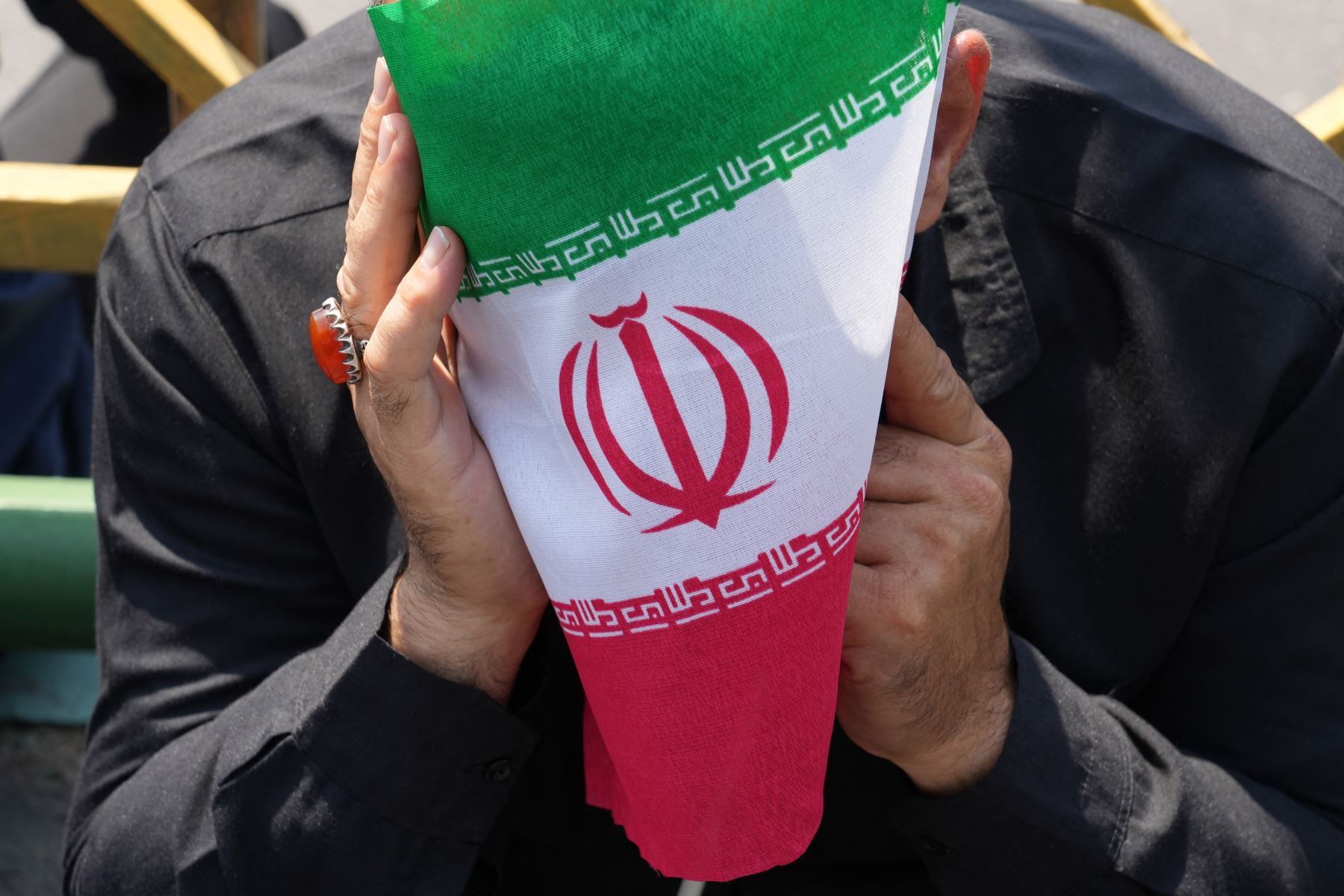 Un ciudadano iraní se cubre el rostro con una bandera de Irán en señal de duelo, durante el paso de la procesión fúnebre del presidente de la república islámica, Ebrahim Raisi, en Teherán, el 22 de mayo de 2024. Foto: AFP