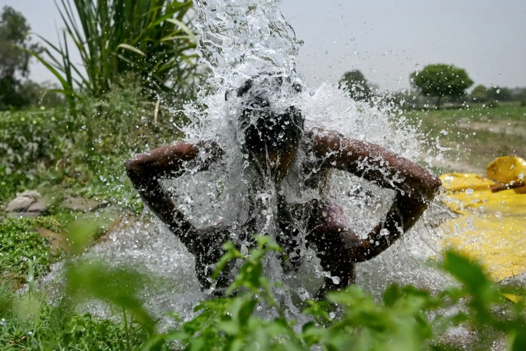 Un hombre se ducha bajo el agua que sale de una tubería a lo largo de las llanuras aluviales de Yamuna en una calurosa tarde de verano en Nueva Delhi. Foto: AFP