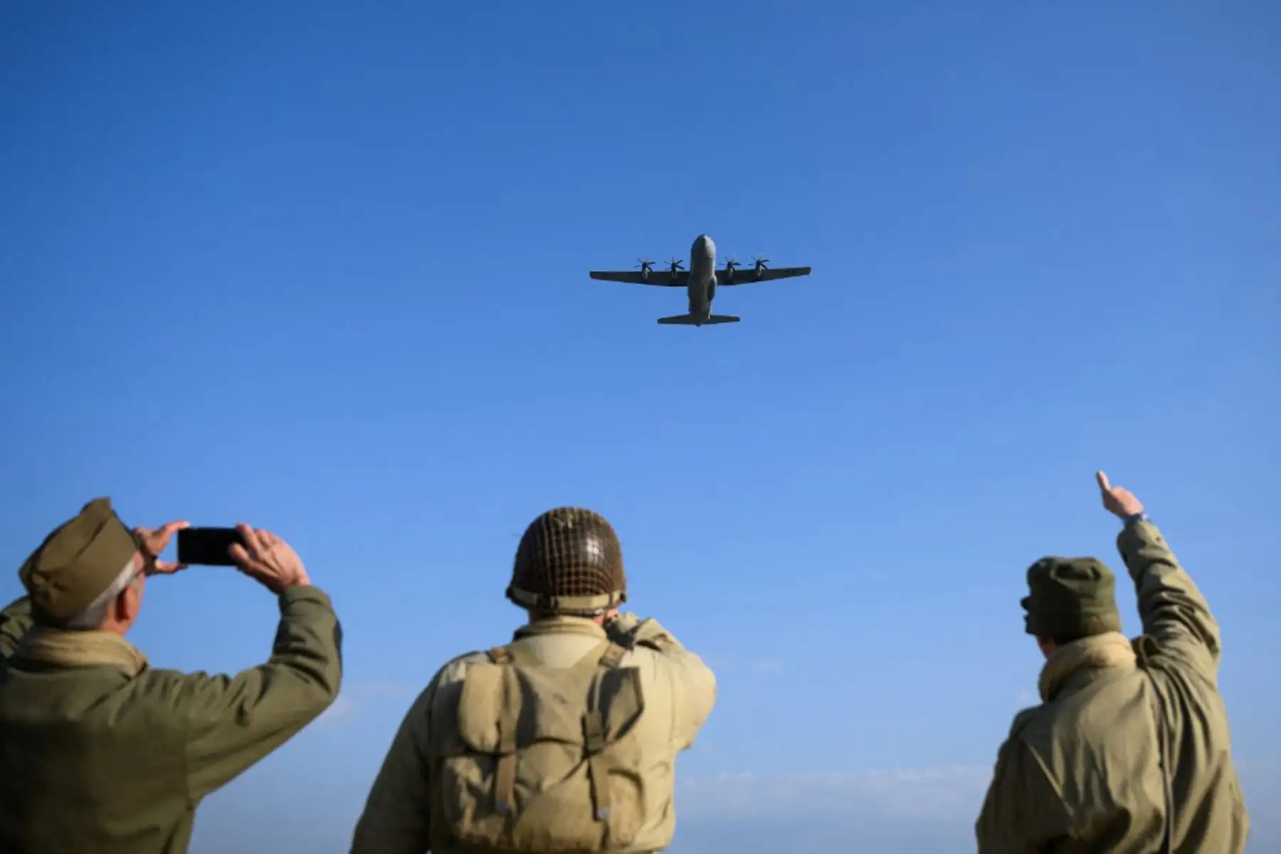 Entusiastas vestidos con una réplica del atuendo militar de la Segunda Guerra Mundial del ejército de los EE. UU. reaccionan cuando un avión Lockheed C-130 Hércules sobrevuela la playa de Utah el 6 de junio de 2024, como parte de las conmemoraciones del "Día D" que marcan el 80 aniversario de los Aliados de la Segunda Guerra Mundial. Foto: AFP