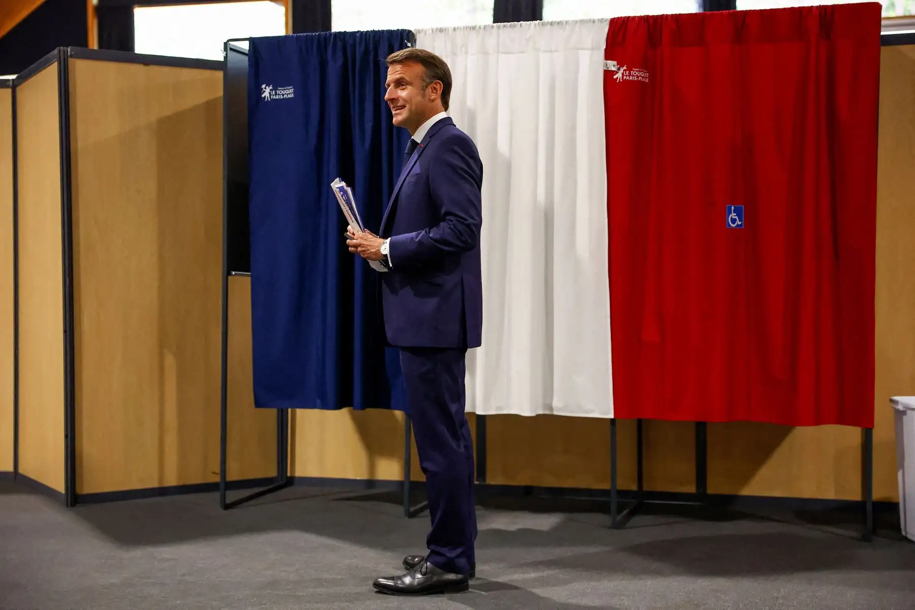 El presidente de Francia, Emmanuel Macron, se encuentra frente a una cabina electoral, adornada con cortinas que muestran los colores de la bandera de Francia, antes de emitir su voto para las elecciones al Parlamento Europeo en un colegio electoral en Le Touquet, al norte de Francia.
Foto: AFP