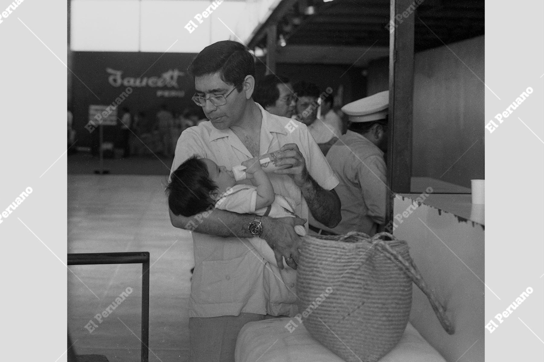 Callao - 26 abril 1983 / Padre de familia le da el biberón a su pequeño hijo, dentro de las instalaciones del Aeropuerto Jorge Chávez. Foto: Archivo Histórico El Peruano