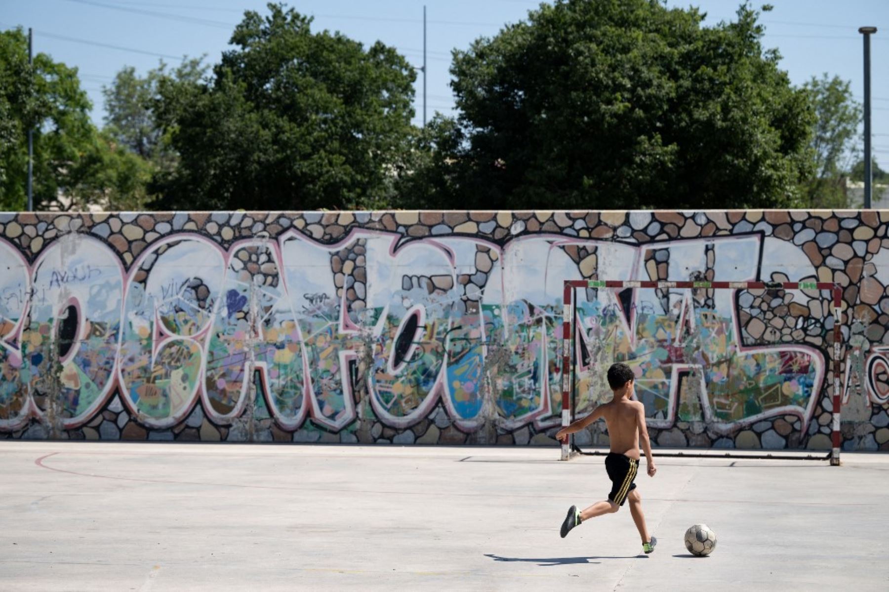 Un niño juega al fútbol junto a un graffiti que dice "Rocafonda", el nombre del barrio donde creció el delantero español Lamine Yamal, en Mataró, a 35 kilómetros de Barcelona. Cada vez que marca un gol, Lamine Yamal suele firmar el número 304 con las manos. Es el código postal del humilde barrio catalán donde pasó parte de su infancia, Rocafonda.

Foto: AFP