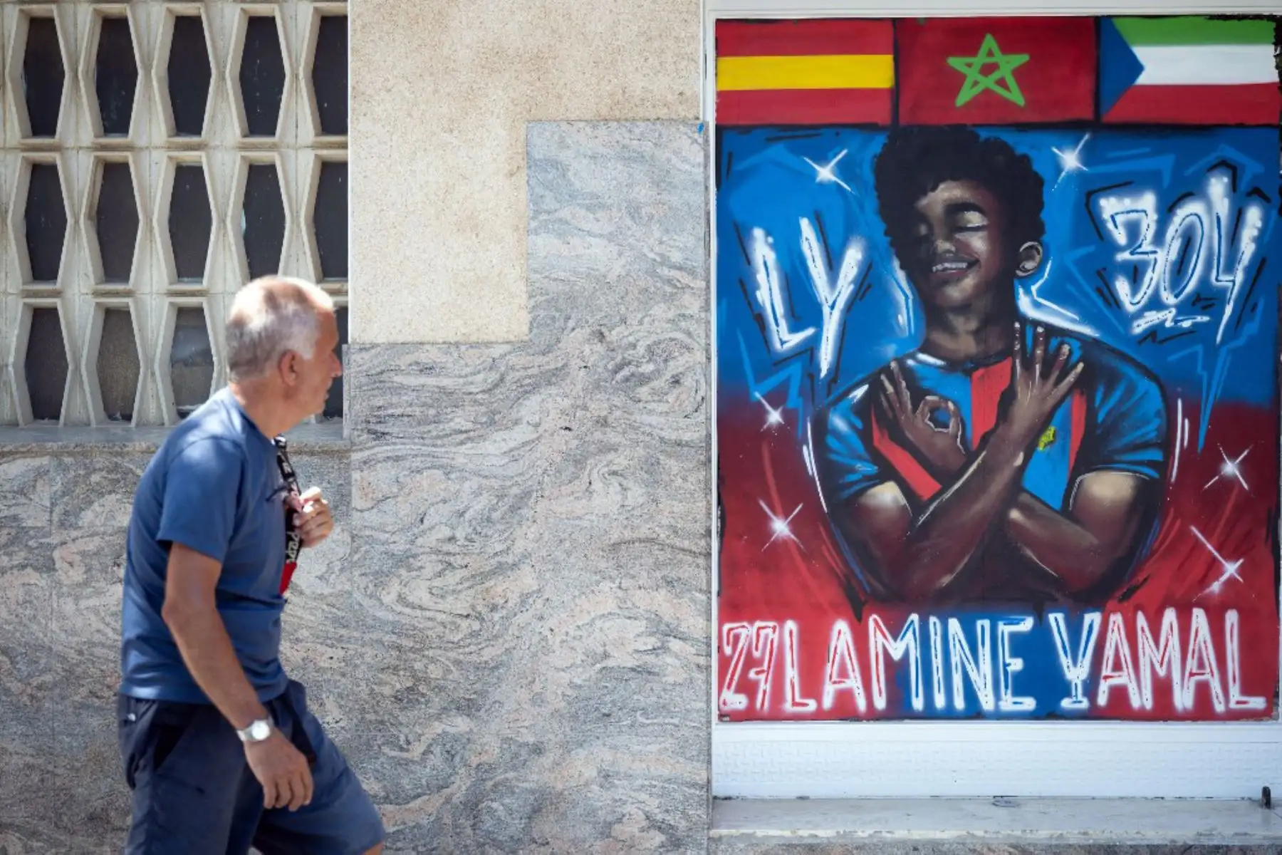 Un hombre pasa junto a un graffiti que representa a Lamine Yamal en Rocafonda, el barrio donde creció el delantero español, en Mataró, a 35 kilómetros de Barcelona. Cada vez que marca un gol, Lamine Yamal suele firmar el número 304 con las manos. Es el código postal del humilde barrio catalán donde pasó parte de su infancia, Rocafonda.

Foto: AFP