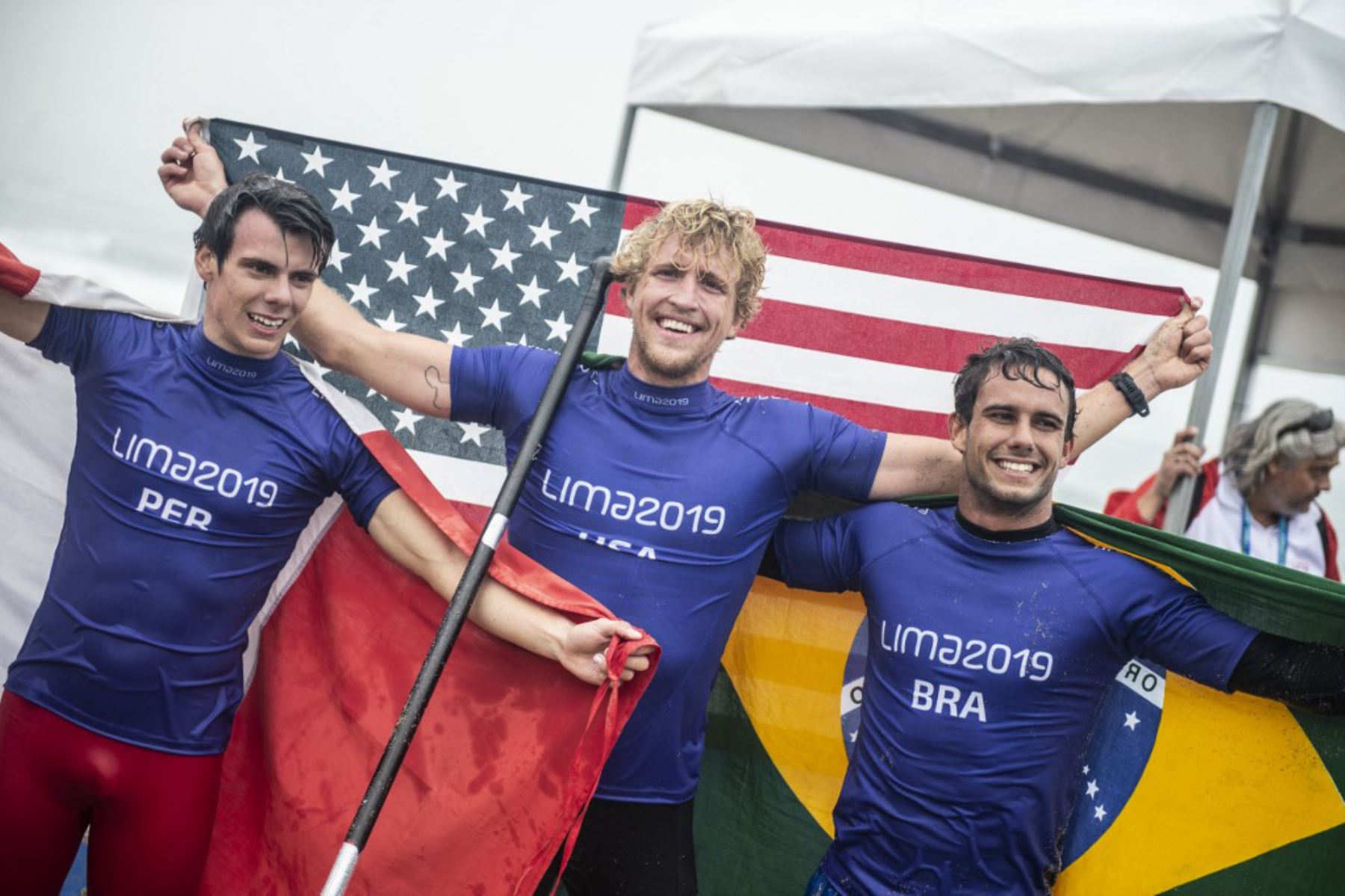 Itzel Delgado de Perú, Connor Baxter de EE. UU. y Vinnicius Martin de Brasil celebran después de ganar sus medallas de bronce, oro y plata respectivamente, en la carrera de SUP masculino de los Juegos Panamericanos Lima 2019 en Lima, el 2 de agosto de 2019. Foto: AFP