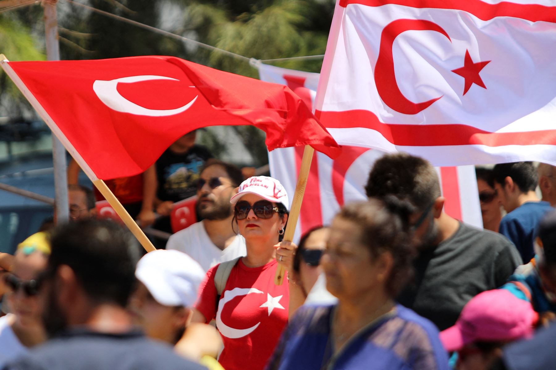 La gente ondea una bandera turca (izq.) y la autoproclamada República Turca del Norte de Chipre (TRNC) durante un desfile militar, mientras Chipre conmemora los 50 años desde que las tropas turcas invadieron la isla mediterránea, en la parte norte de la dividida capital de Chipre, Nicosia, en julio. 20, 2024. Foto: AFP