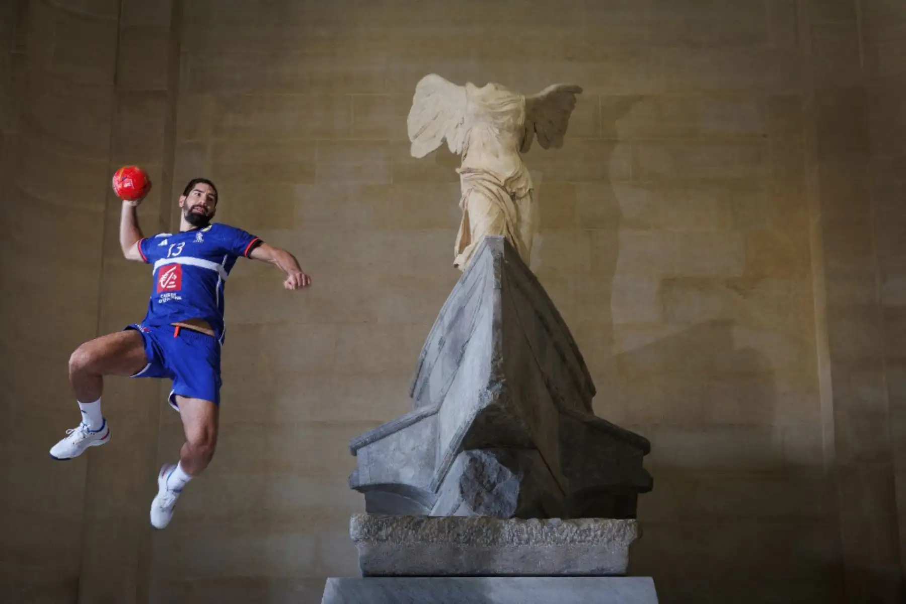 El lateral izquierdo de balonmano de Francia, Nikola Karabatic, salta junto a la escultura griega de la época helenística, "Victoria alada de Samtracia", en lo alto de la escalera principal del Museo del Louvre en París. Foto: AFP