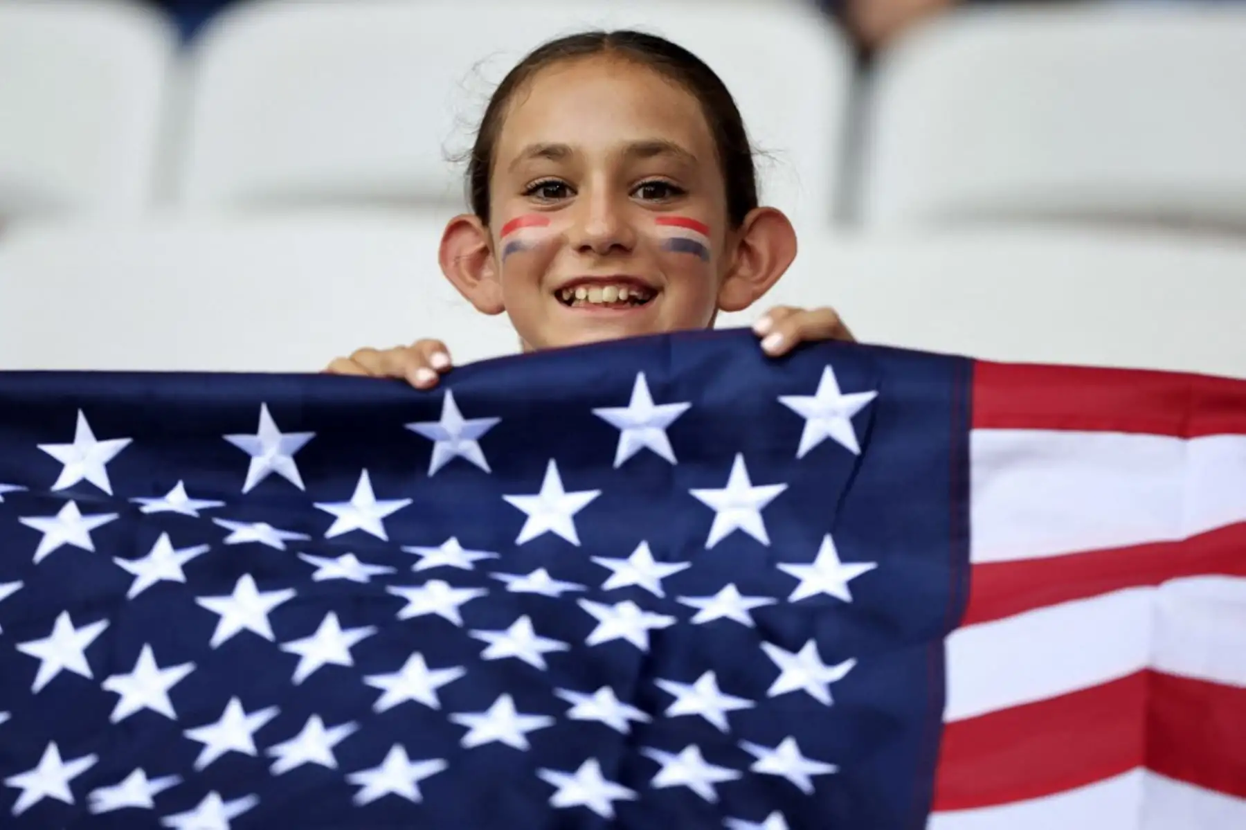 Una aficionada de Estados Unidos sonríe detrás de una bandera antes del partido de fútbol femenino del grupo A entre Estados Unidos y Zambia durante los Juegos Olímpicos de París 2024 en el Estadio de Niza el 25 de julio de 2024. Foto: AFP