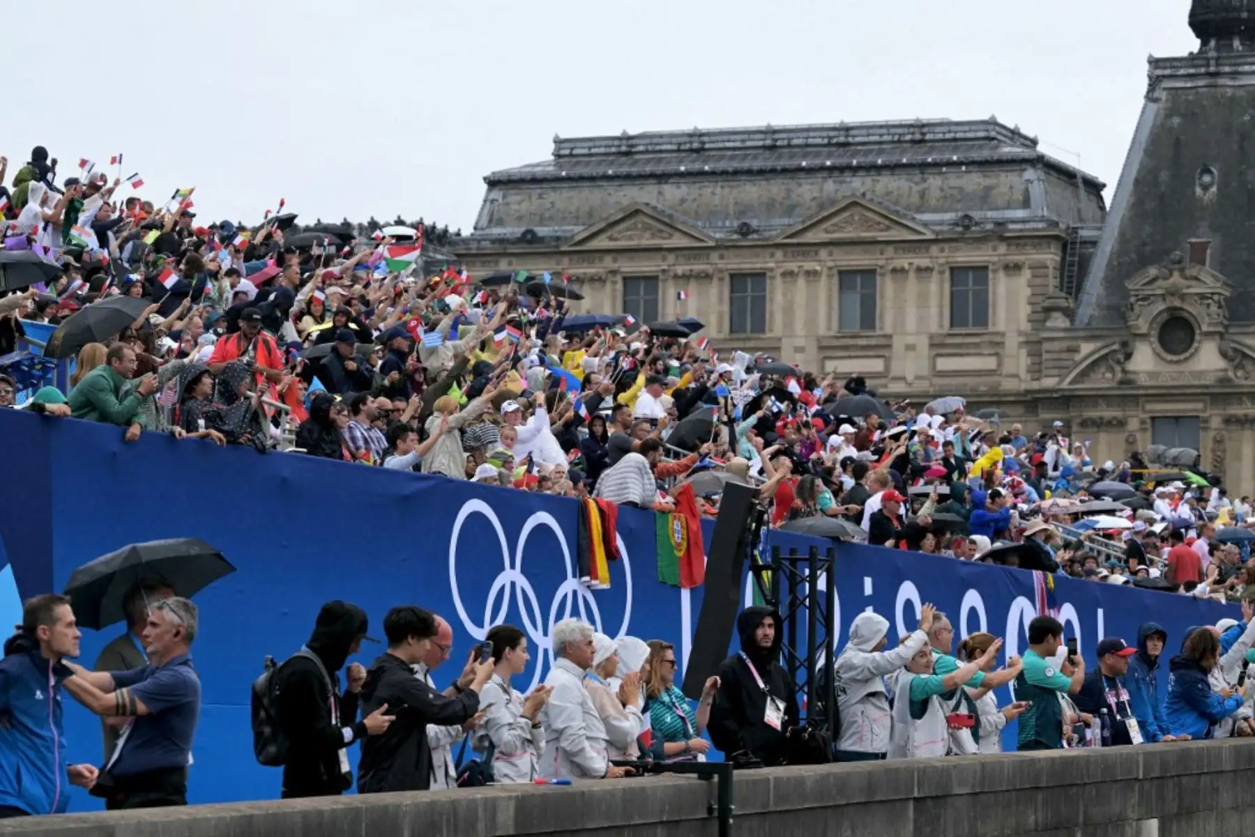 Los espectadores saludan con banderas a las delegaciones de atletas desde el Pont du Carrousel durante la ceremonia de inauguración de los Juegos Olímpicos de París 2024, el 26 de julio, mientras se ve como fondo el Museo del Louvre. Foto: AFP
