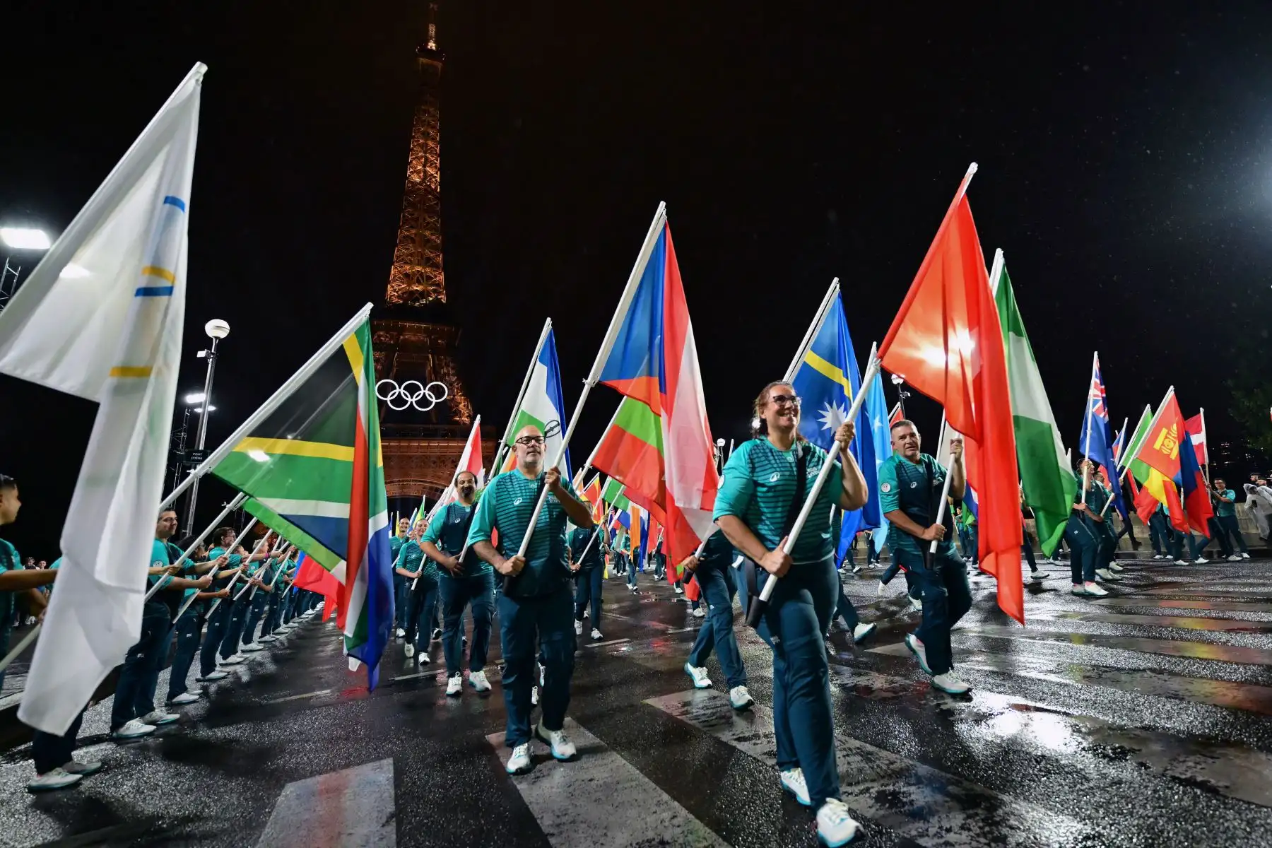 Los voluntarios llevan las banderas de los equipos olímpicos en el puente Iena durante la ceremonia de apertura de los Juegos Olímpicos de París 2024 en Francia el 26 de julio, mientras se ve la Torre Eiffel al fondo. Foto: AFP