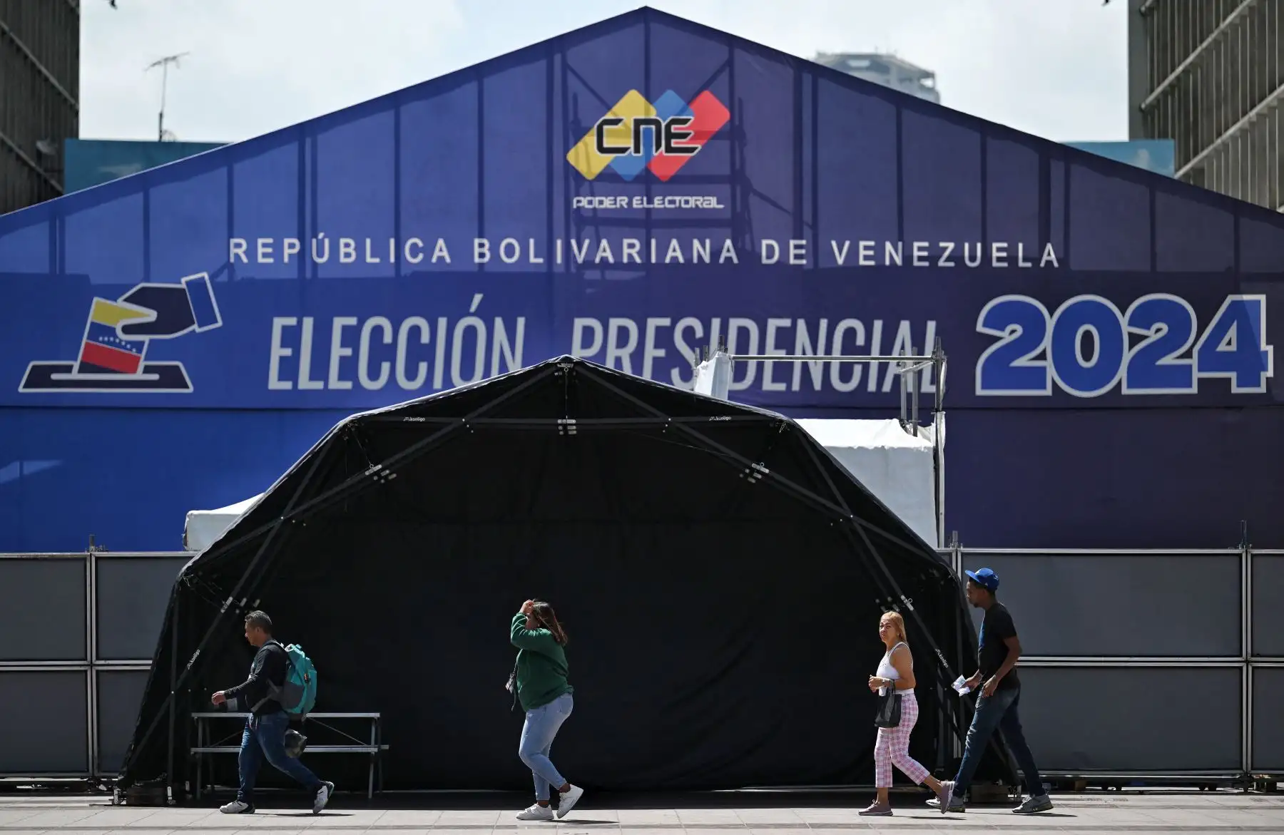 La gente camina frente al centro de medios del Consejo Nacional Electoral (CNE) en Caracas. Venezuela celebrará elecciones presidenciales el 28 de julio de 2024.
Foto: AFP
